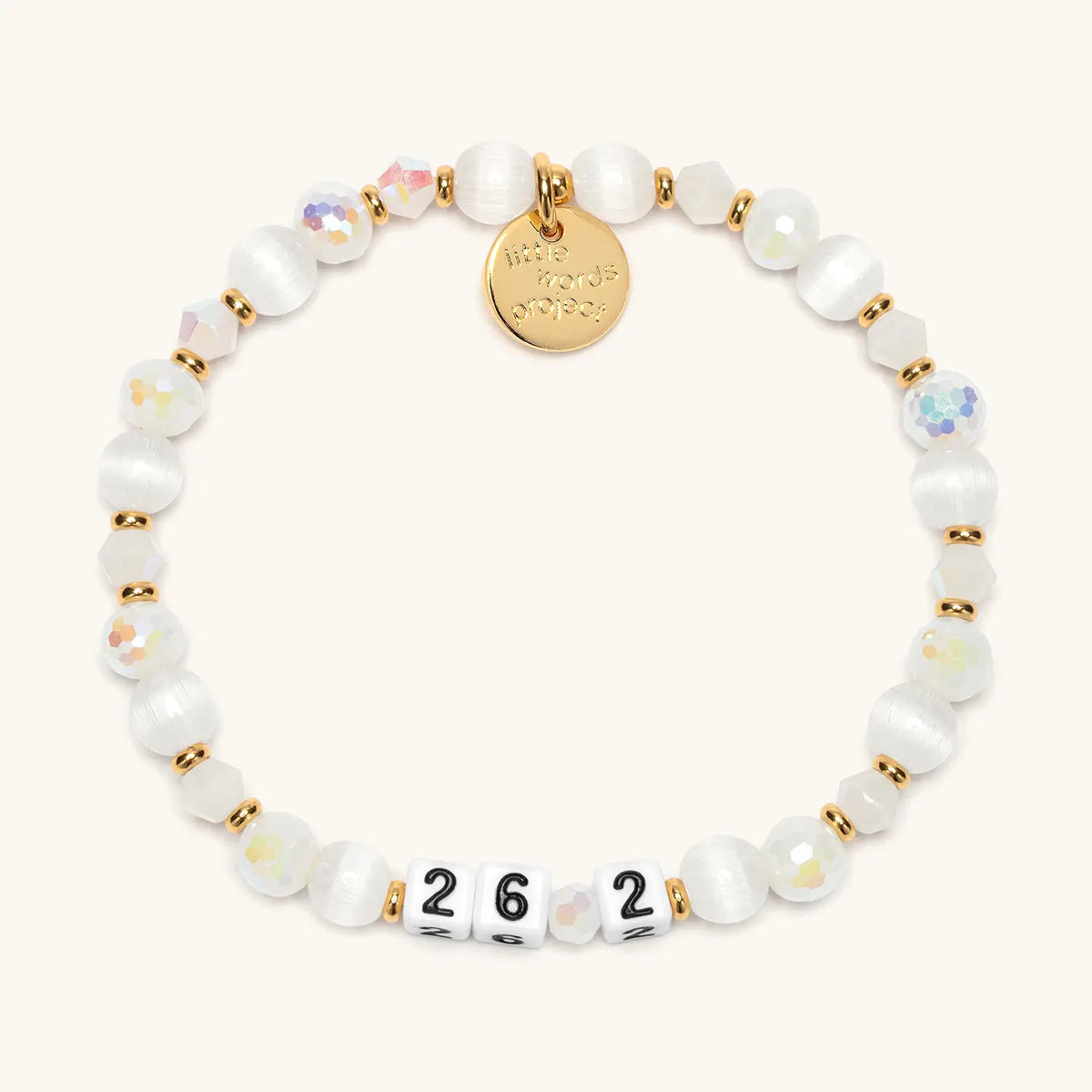 26.2 bracelet in the Snowy Night bead pattern, white number beads with white cat eye beads, iridescent faceted beads, and frosted white crystals with gold accents, flat-lay on cream background