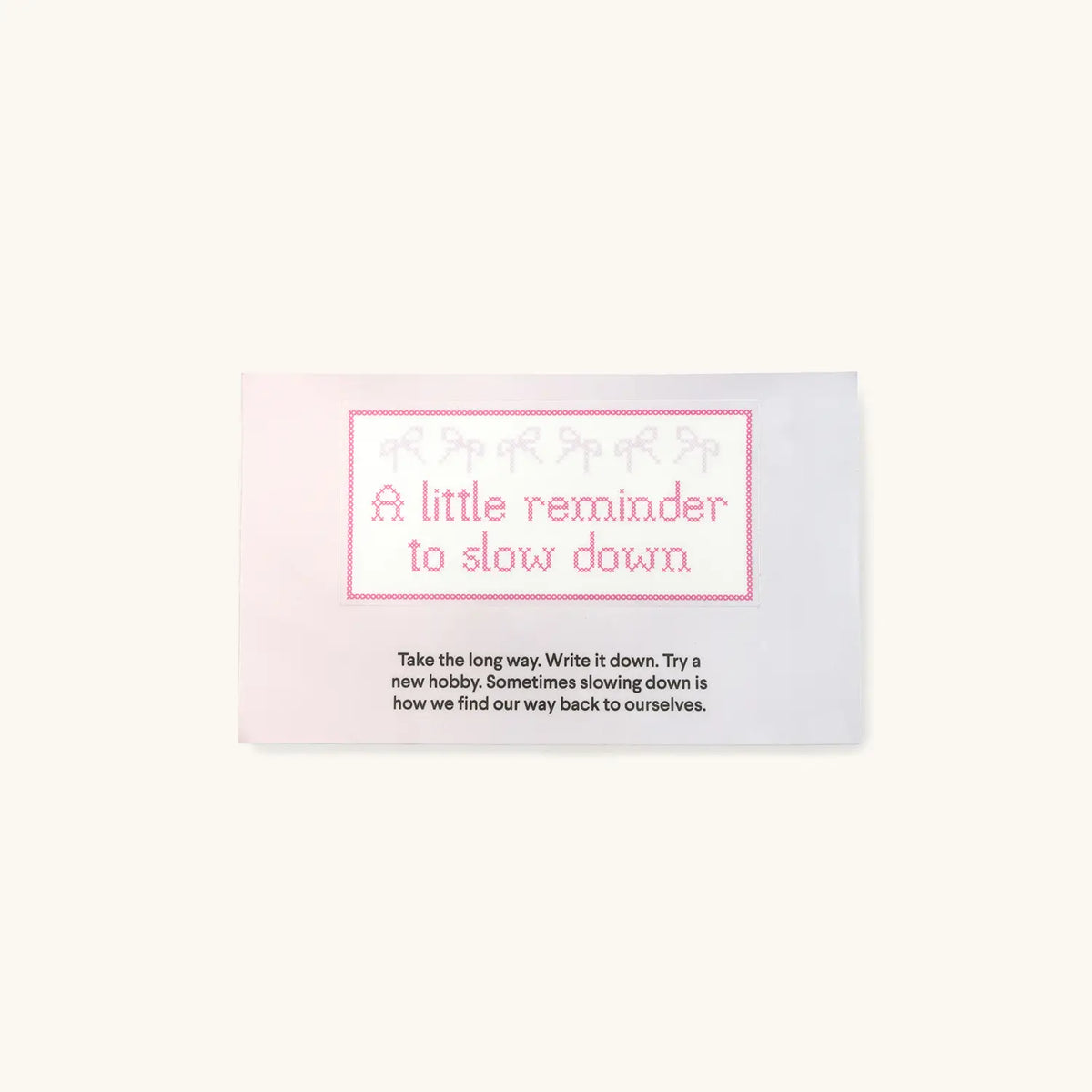 Slow Down October Word of the Month sticker reading A little reminder to slow down in pink cross-stitch lettering with bow border and a short note to take the long way, packaging on cream background