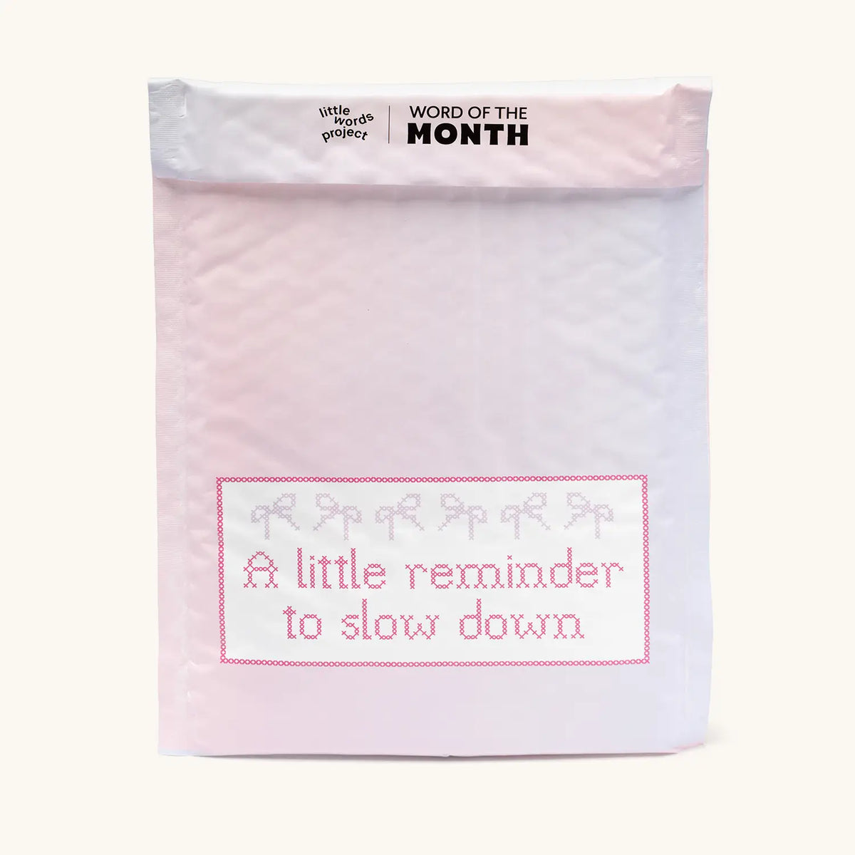 Front of the pink and white Little Words Project Word of the Month bubble mailer with the A little reminder to slow down October sticker, packaging on cream background