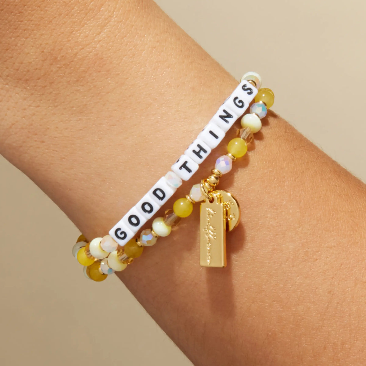 Good Things bracelet by Anna Sitar on wrist, white letter beads with yellow glass and cream beads and a gold Kindfluencer tag, on-model