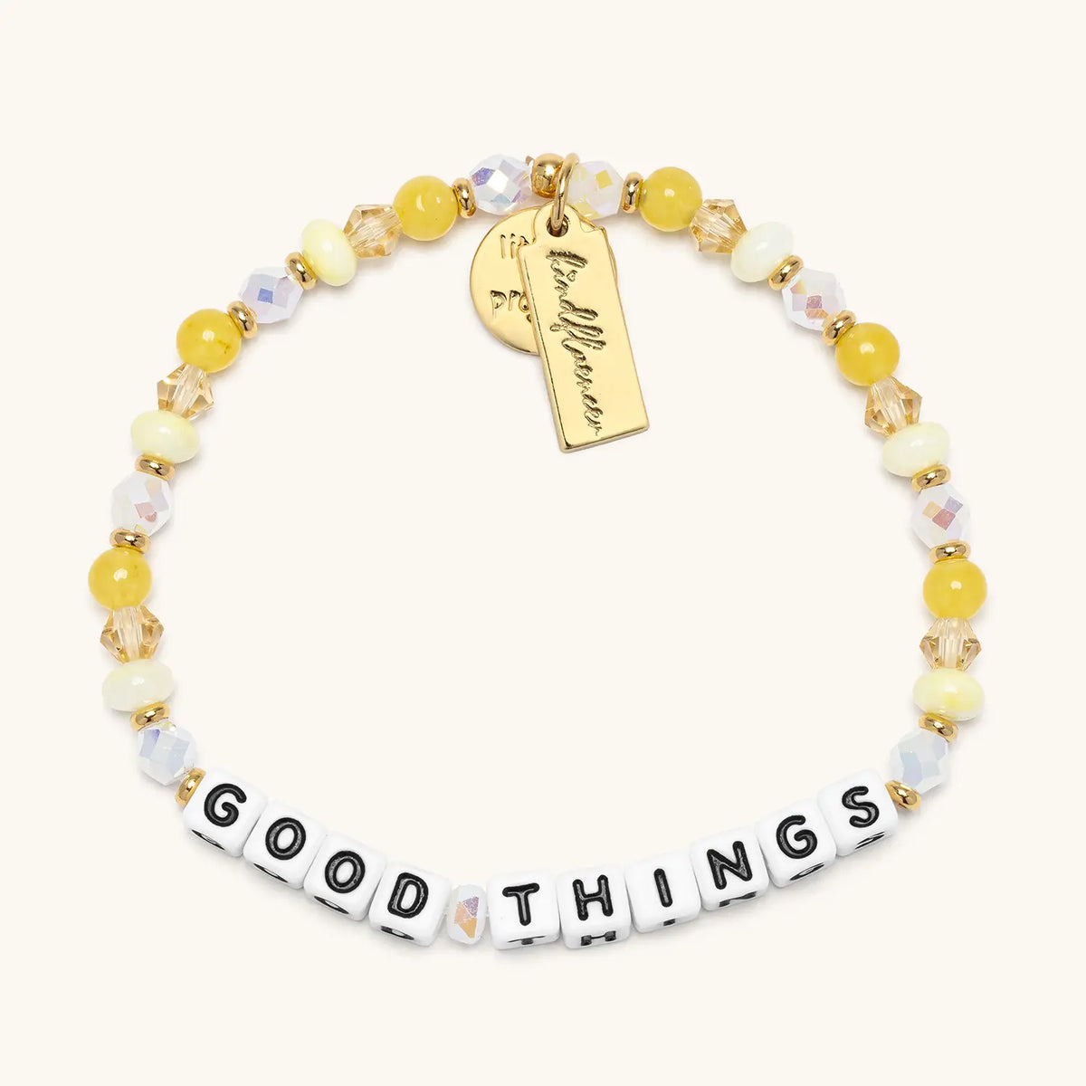 Good Things bracelet by Anna Sitar in the Honeycomb bead pattern, white letter beads with yellow glass, cream mother of pearl, and iridescent crystal beads with a gold Kindfluencer tag, flat-lay on cream background