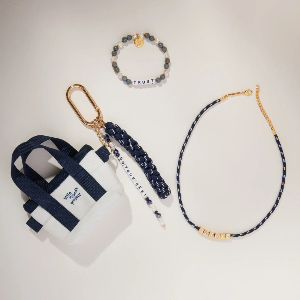 Fall Founder Faves Set flat-lay on cream background showing the Trust bracelet, BOLDER Enough paracord necklace, and Do Your Best Bag Charm with mini canvas tote and navy paracord tassel