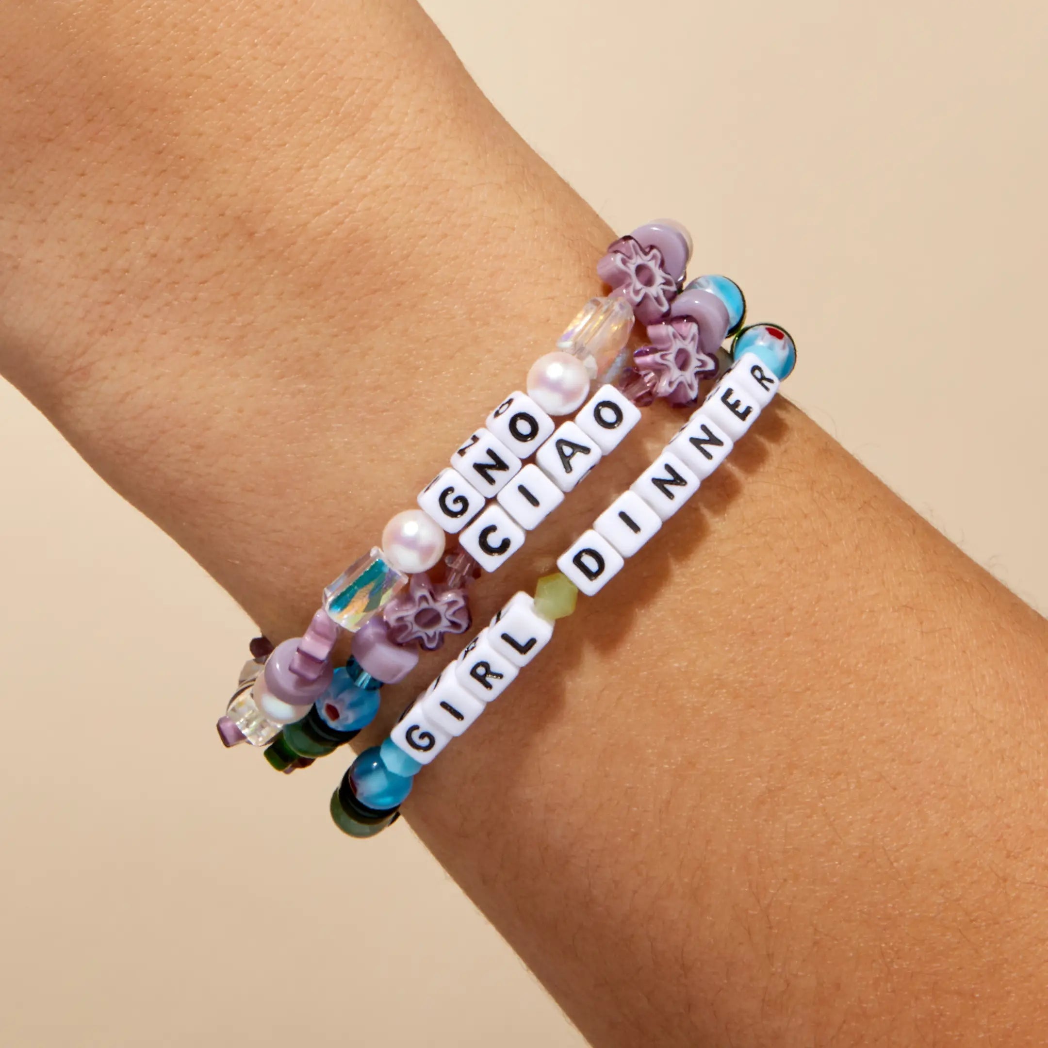 Bracelets with letter beads on a wrist against a beige background