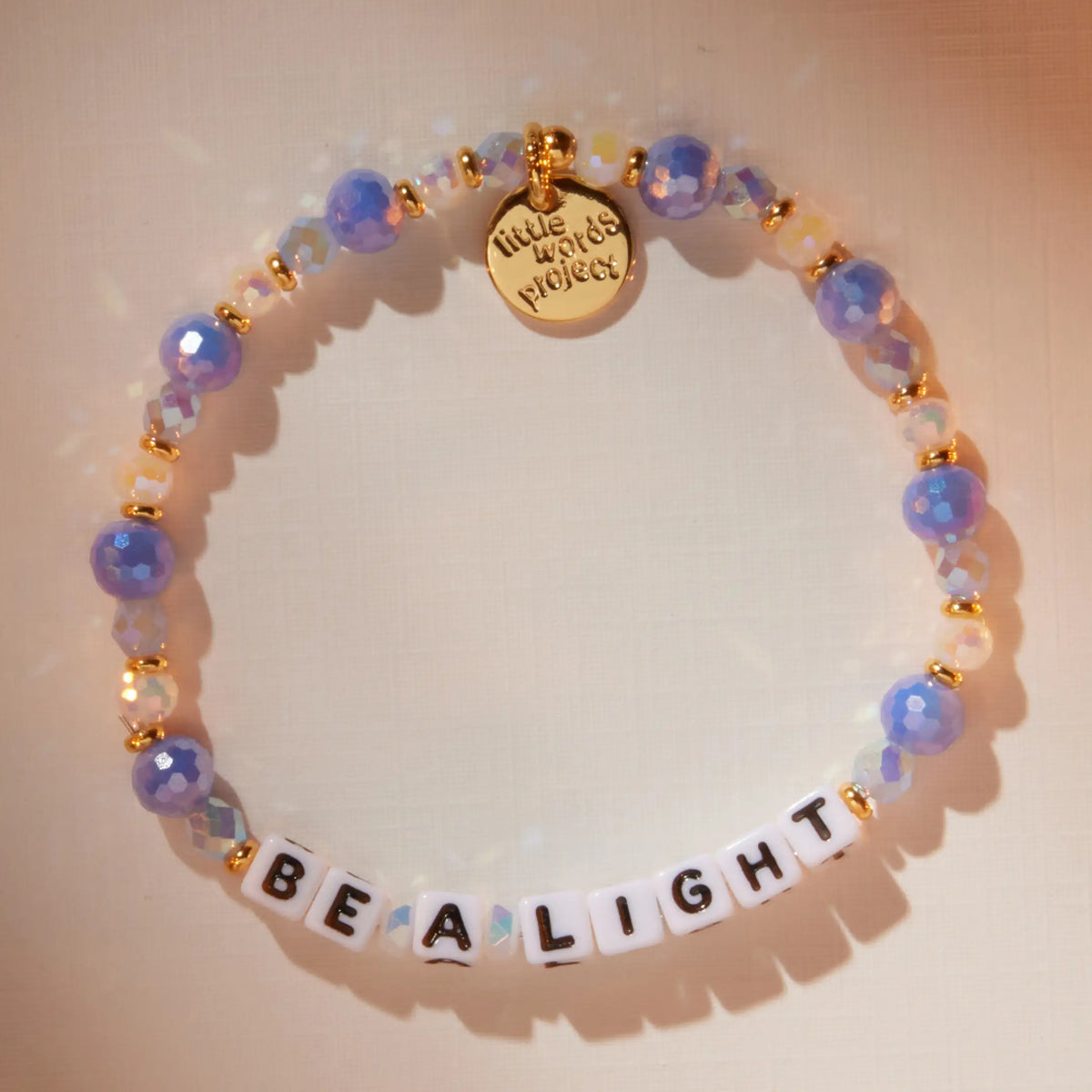 Be a Light bracelet in the Blizzard Baby bead pattern with white letter beads, flat-lay on warm neutral background with soft light