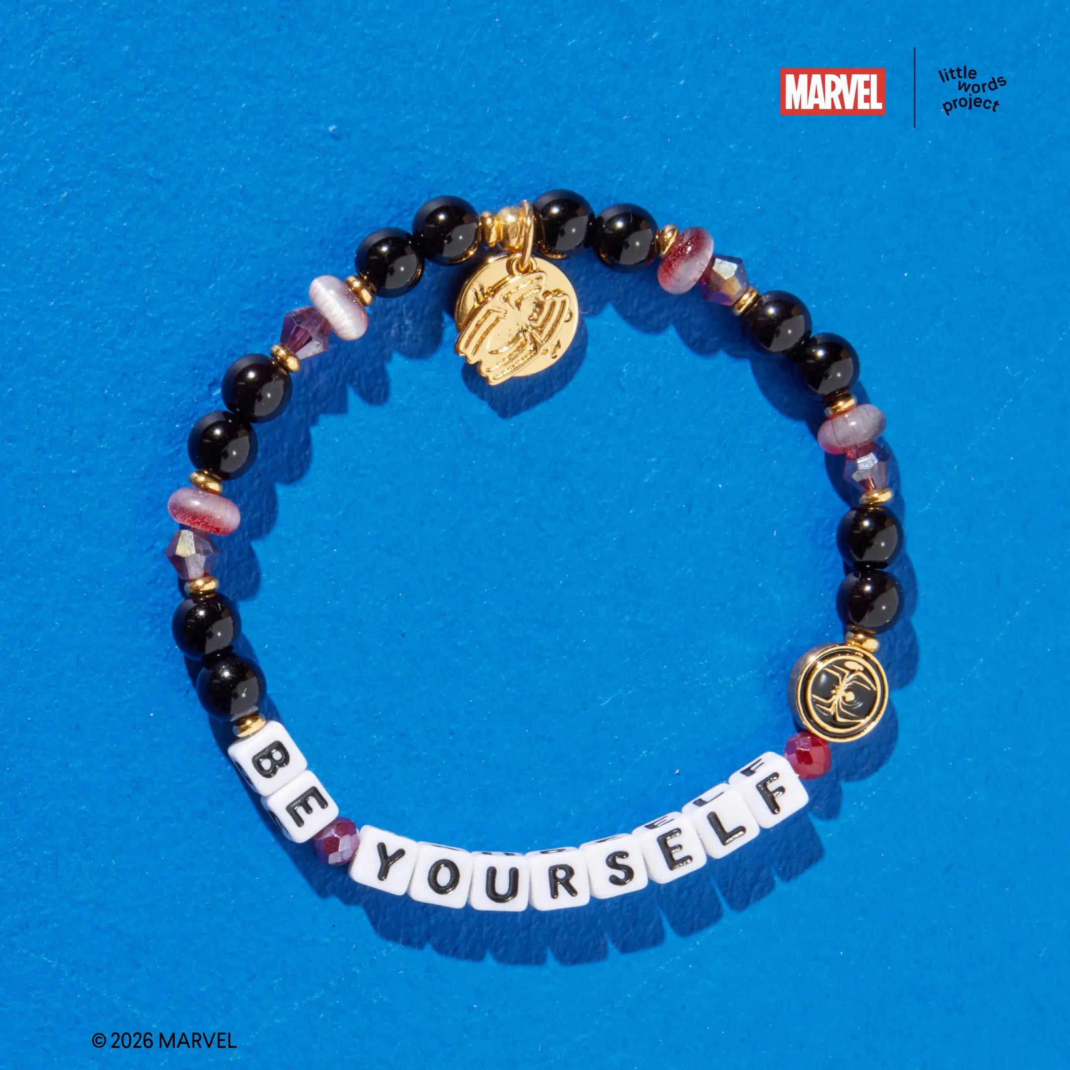 Be Yourself bracelet from Marvel's Spider-Man collection, flat-lay on blue background, black glass beads with mauve cat eye beads and gold Spider-Man enamel casted bead