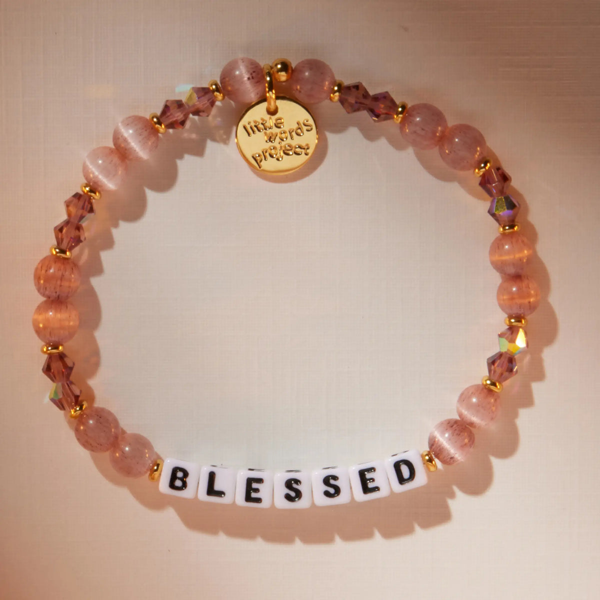 Blessed bracelet in the Holiday Spritz bead pattern with white letter beads, flat-lay on warm neutral background with soft light