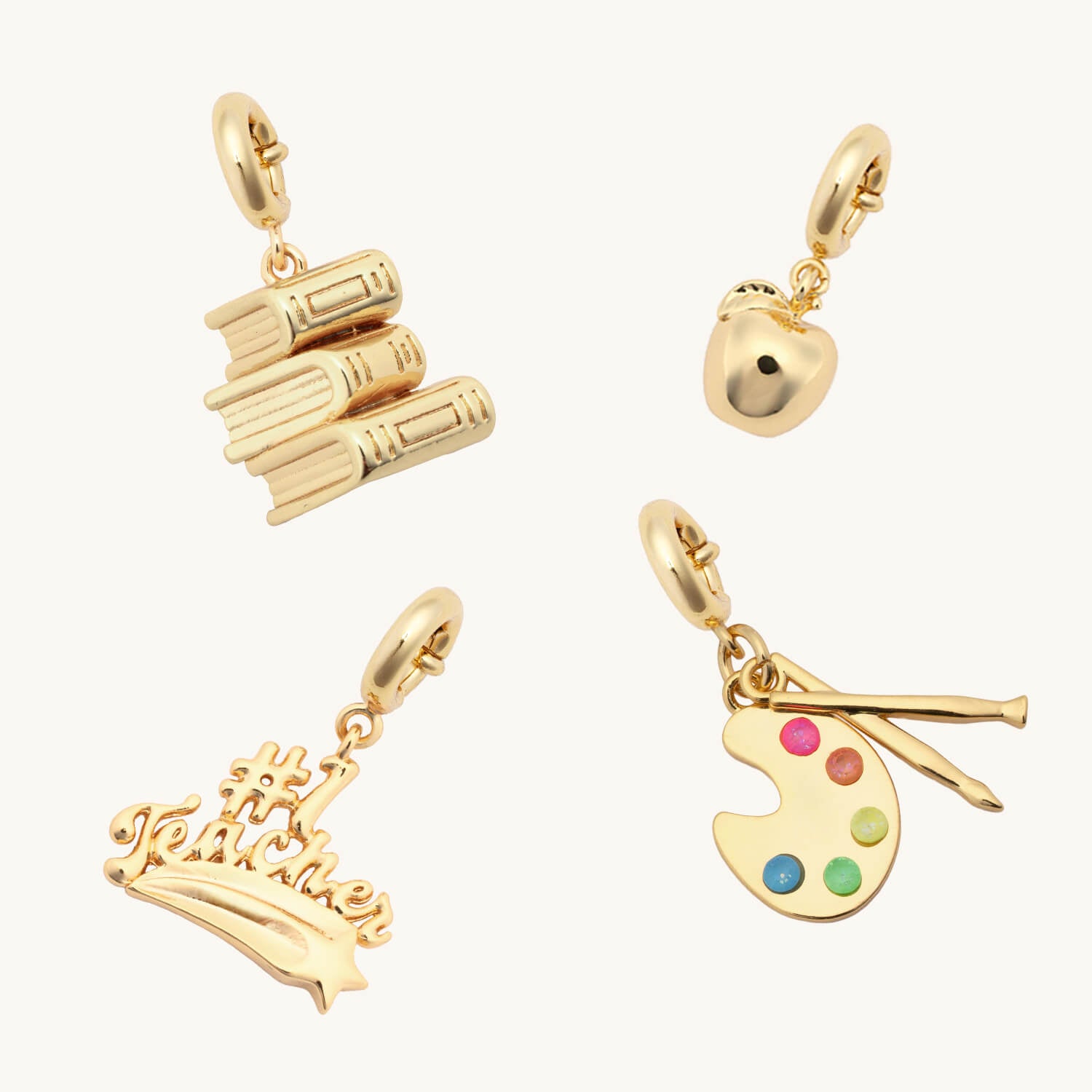 Set of gold charms including books, an apple, a colorful palette, and a #1 Teacher on a white background.