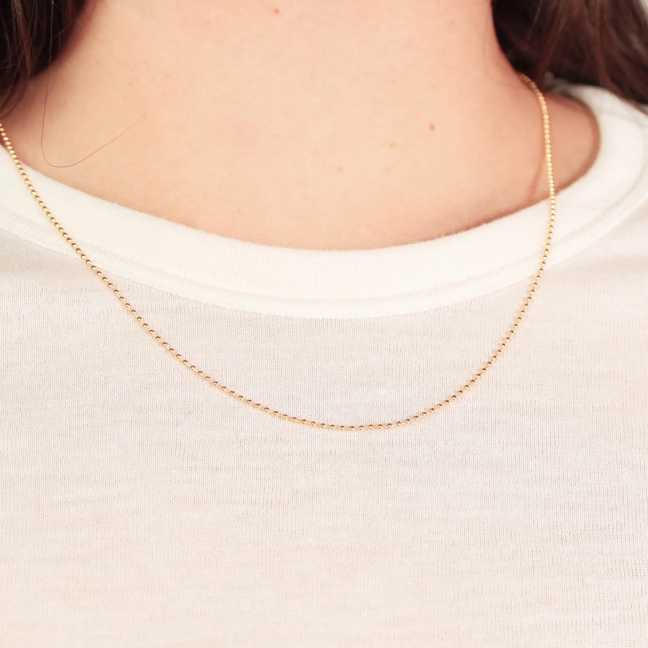 Gold necklace on a person wearing a white shirt