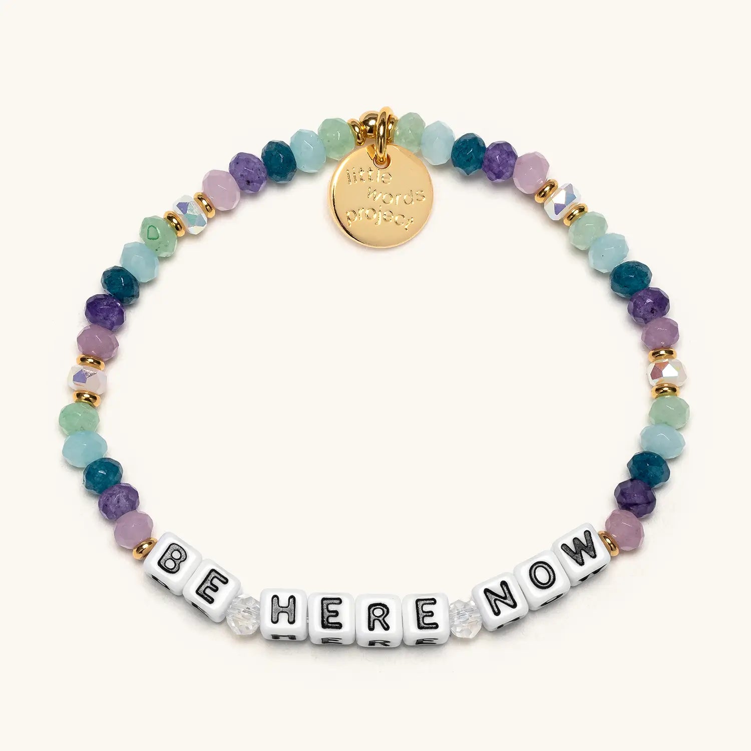 Multicolored beaded bracelet with a gold tag and 'BE HERE NOW' message on a white background