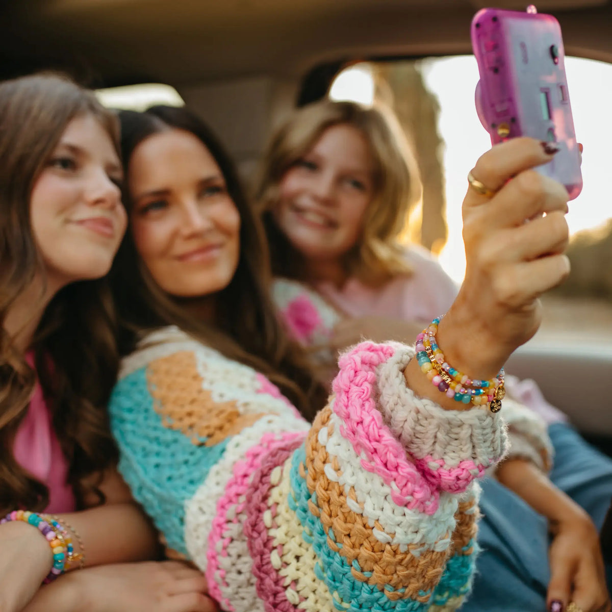 Three friends taking a selfie in the back seat, close up of the LWP x Britt Horton Fearless Bracelet Set stack with gold letter beads, pastel semi precious stone beads, and a gold charm