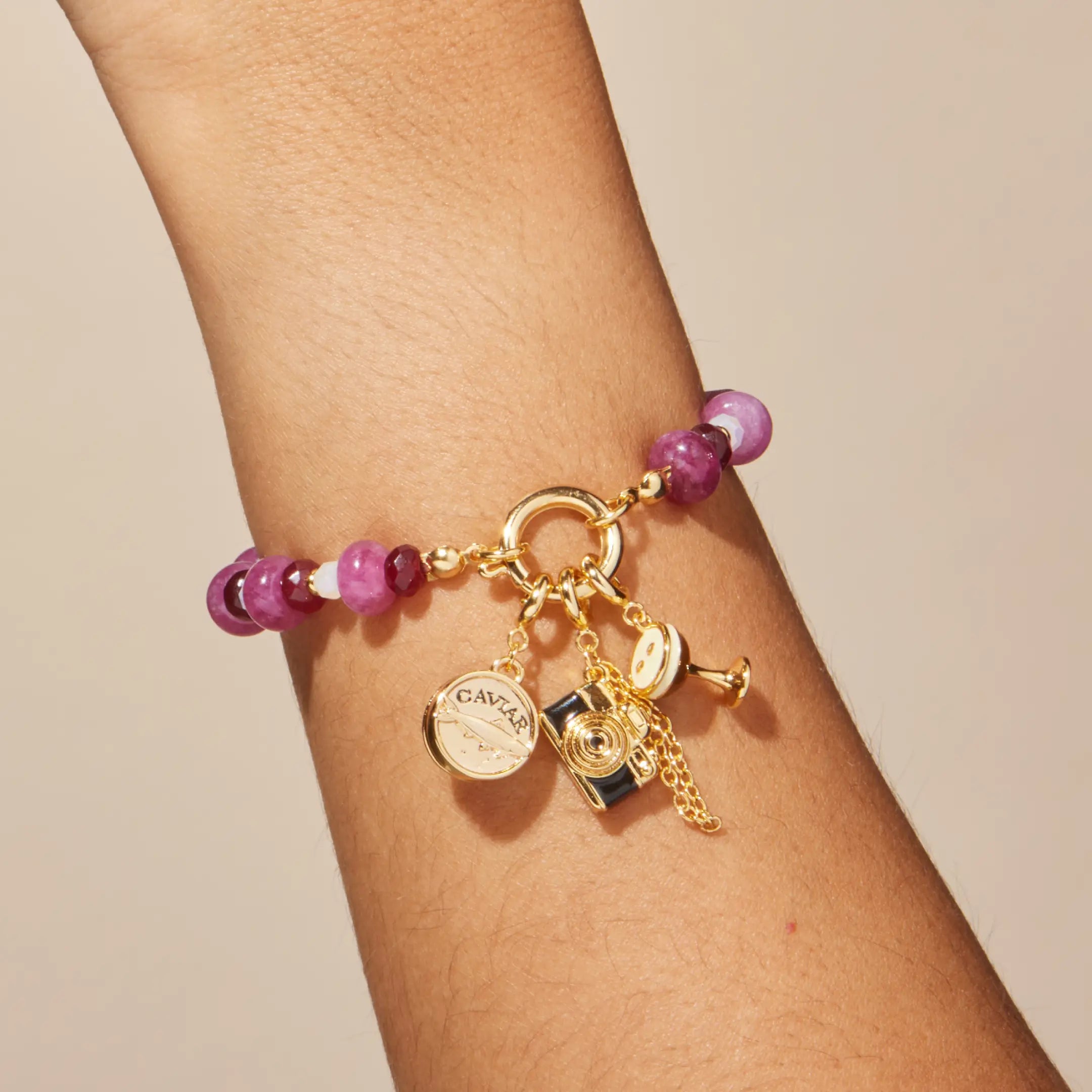 Gold bracelet with purple beads and charms on a wrist against a beige background