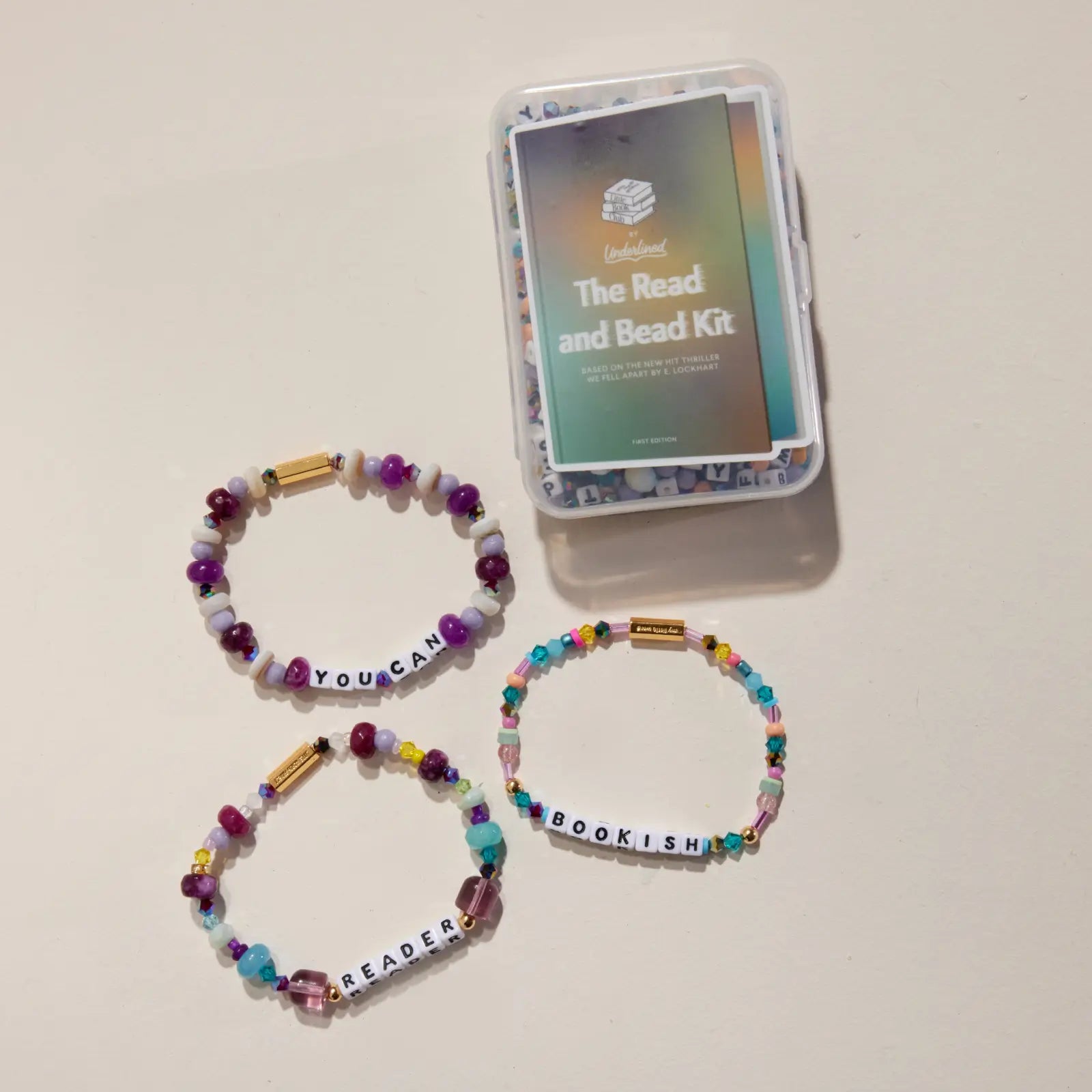 Three colorful beaded bracelets with motivational phrases and a 'The Read and Bead Kit' packaging on a beige background.