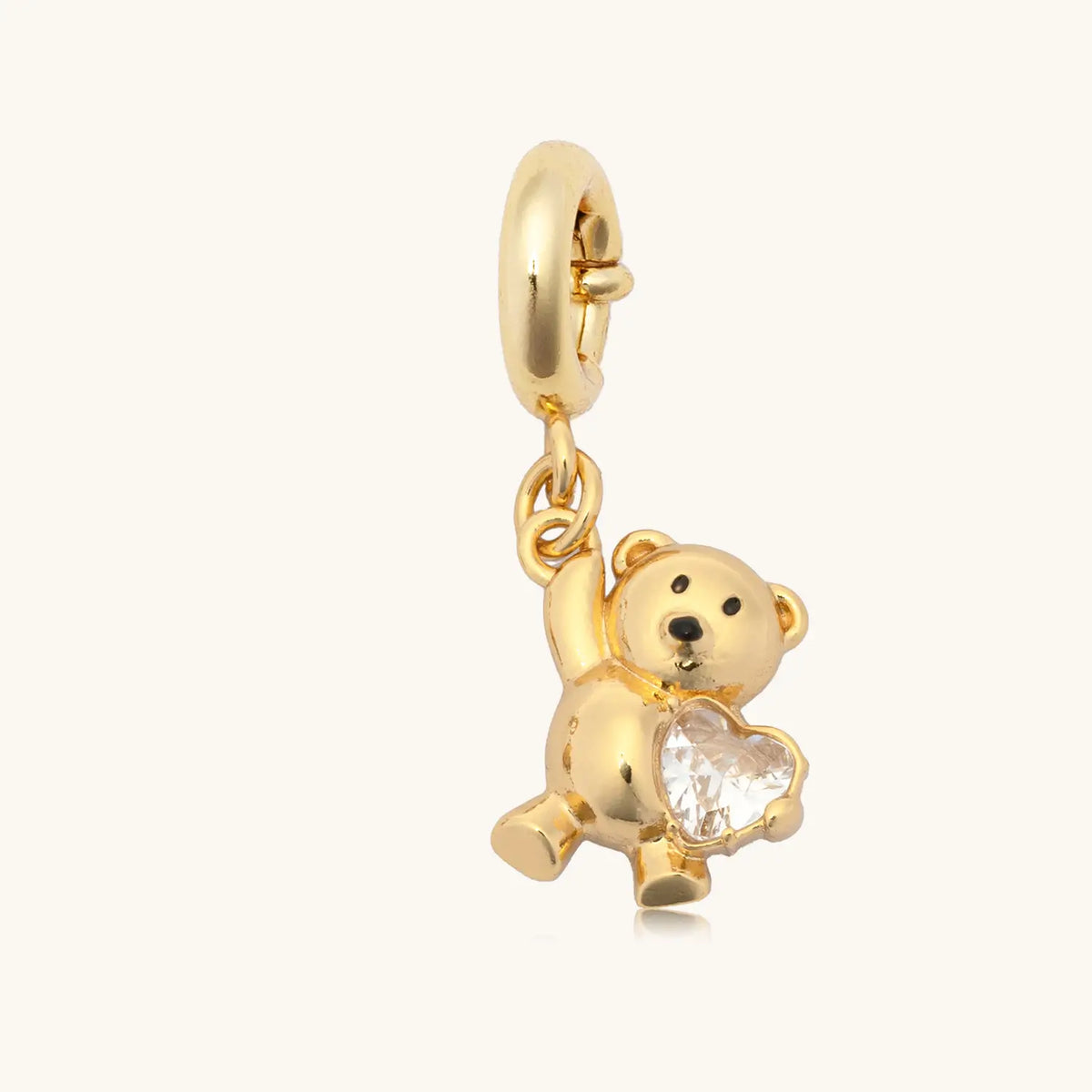 Teddy Bear Gem Charm from the Golden Cherry Charm Bracelet set, gold teddy bear holding a cz heart, flat-lay on cream background