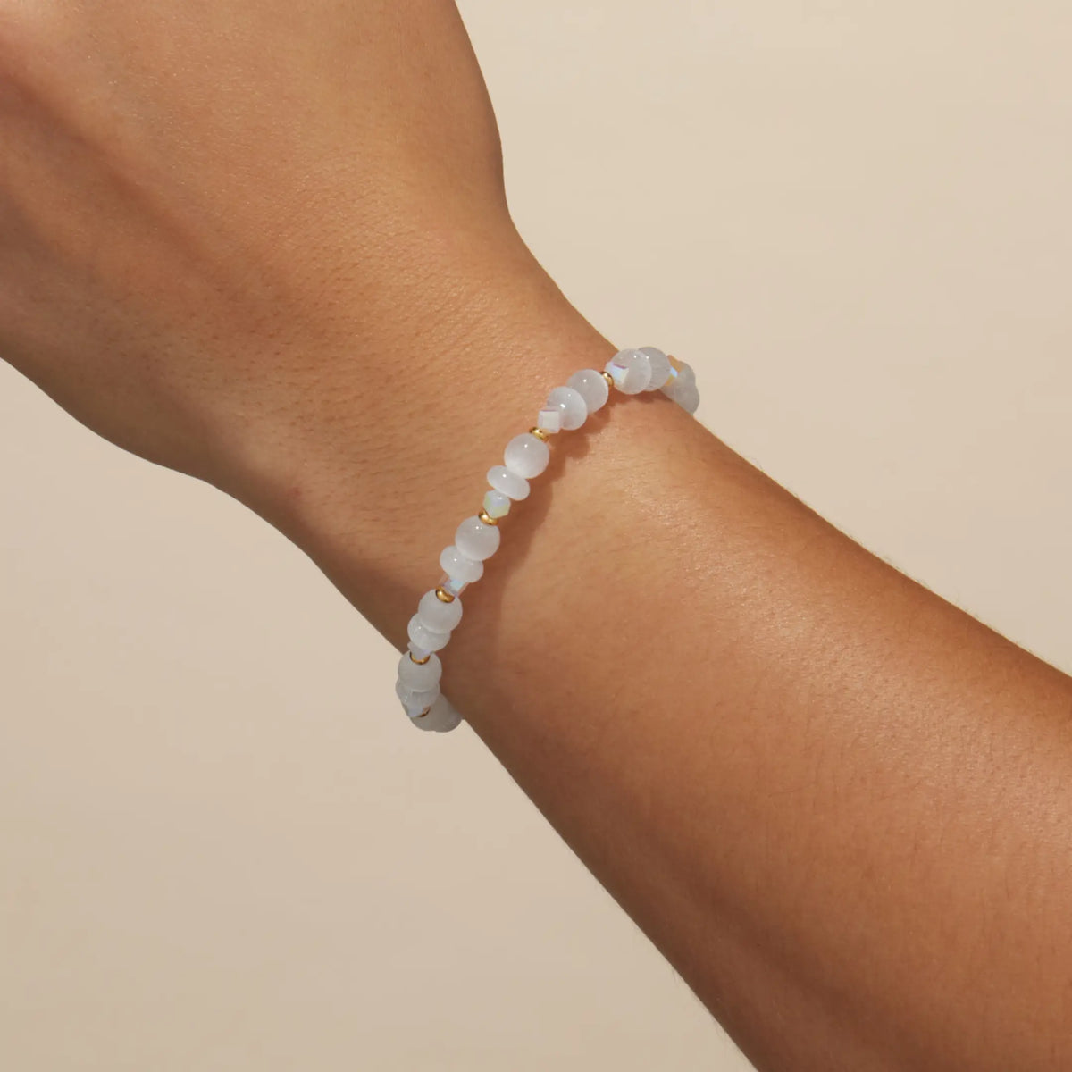 Arctic Honey Bracelet Base worn on a wrist, milky white cat eye and clear crystal beads, on-model on a tan background