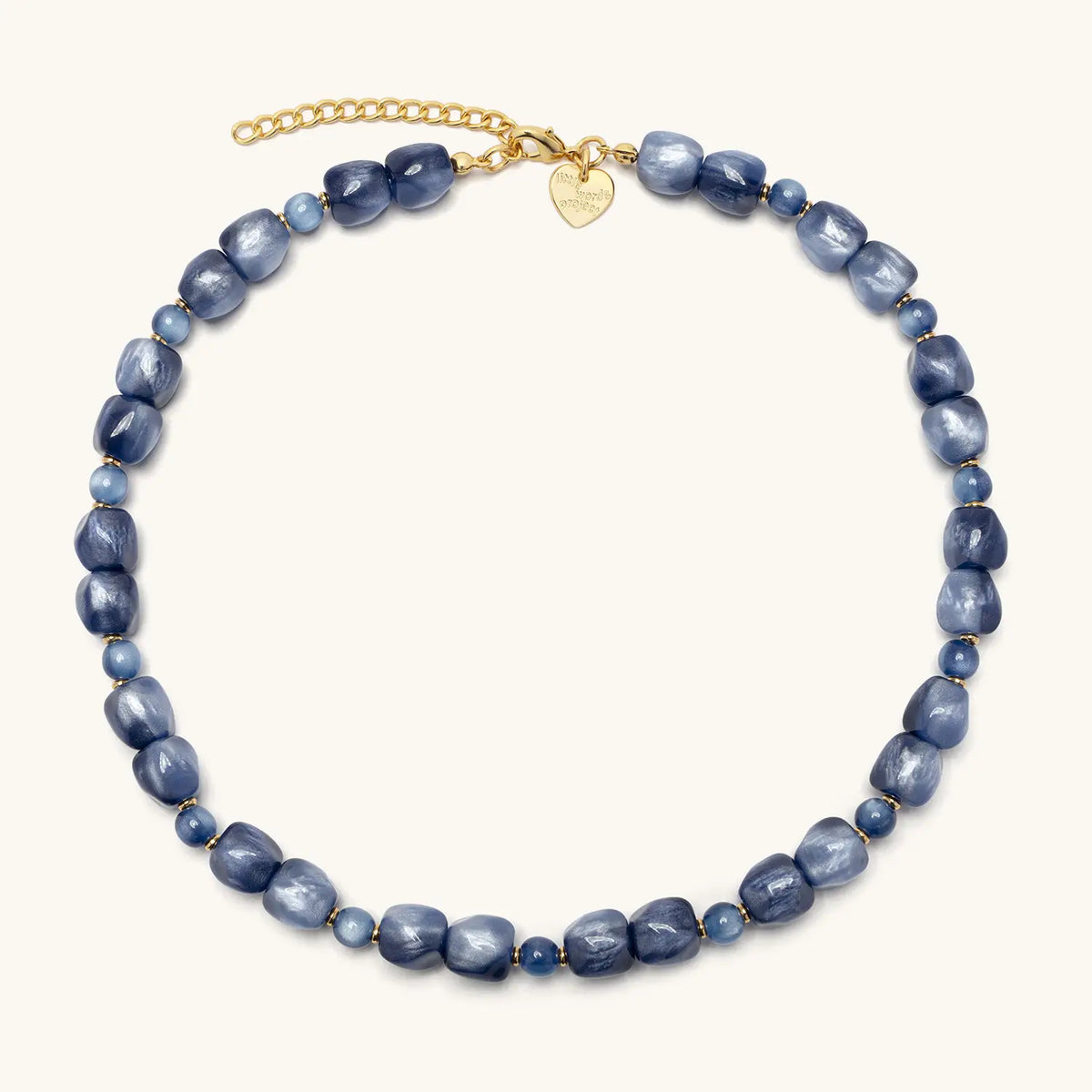 Radio Fever Necklace laid flat in a circle, shimmery blue beads with a gold extender chain and gold heart logo tag, flat-lay on cream background