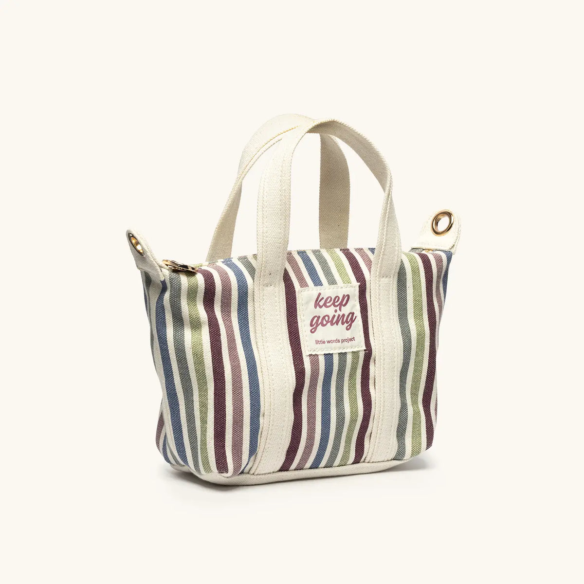 Keep Going Mini Tote, natural canvas mini tote with blue, plum, and green vertical stripes and a pink Keep Going patch, angled view on cream background