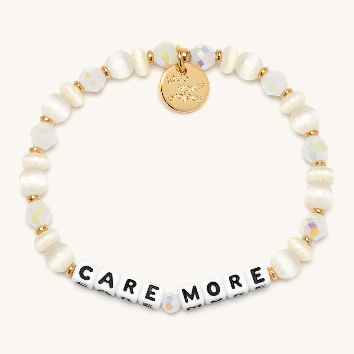 Care More bracelet with white letter beads, ivory cat's eye beads, white AB faceted crystals, and cream pearl-luster rondelles with gold accents, flat-lay on cream background