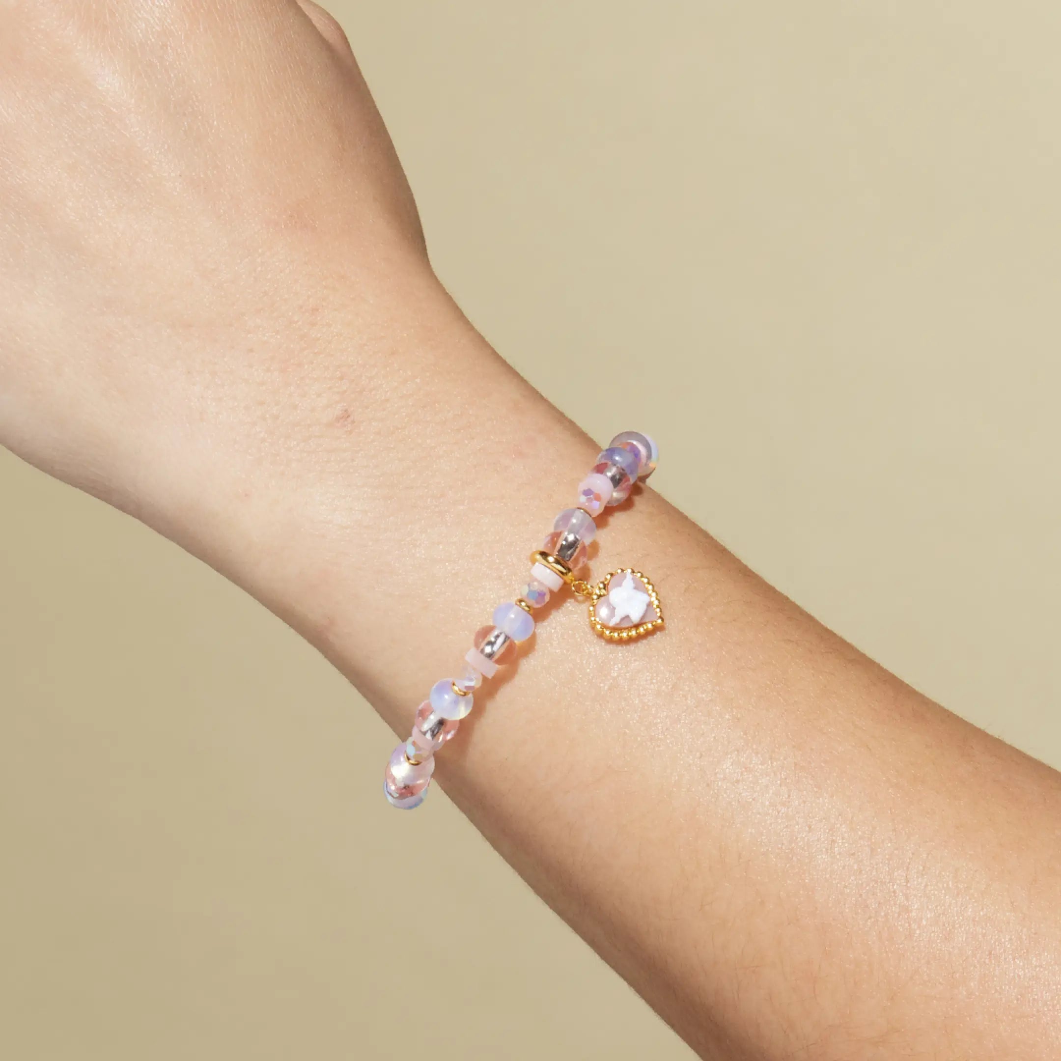 Bracelet with heart charm on a wrist against a beige background