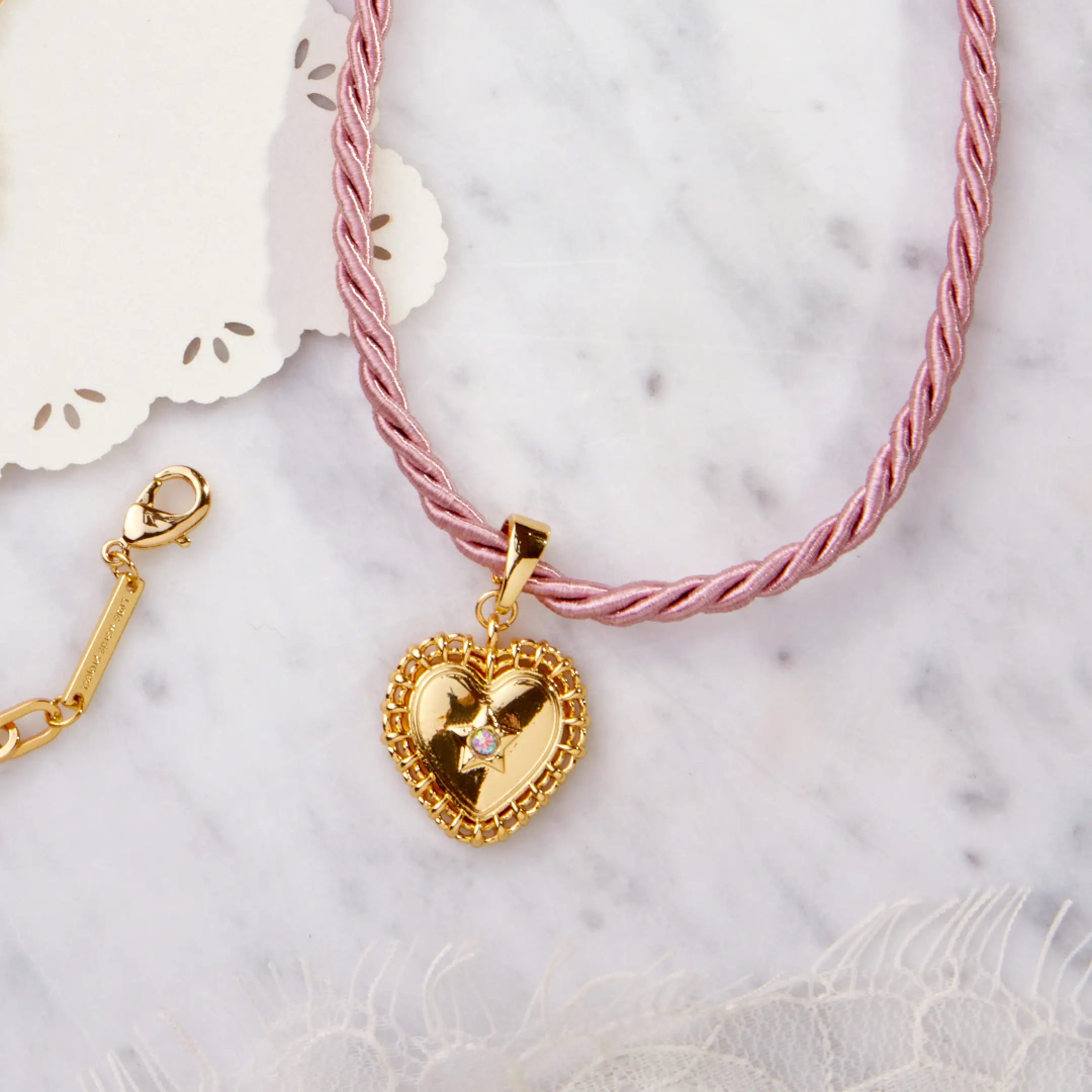 Pink braided necklace with a gold heart-shaped pendant on a marble surface