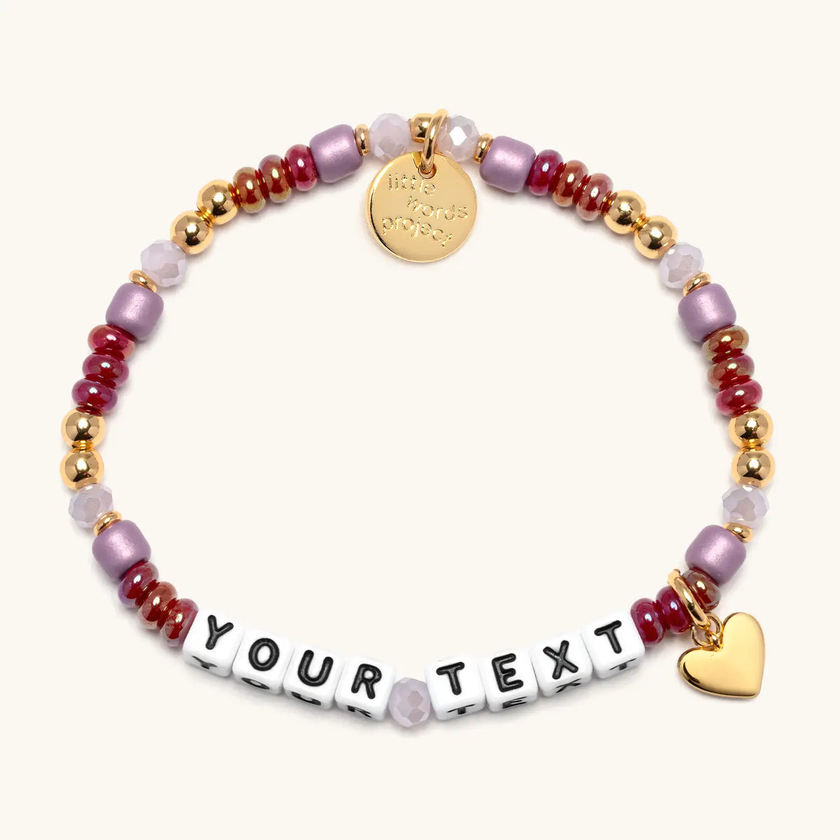 Custom Golden Cherry bracelet in the Golden Cherry bead pattern, white letter beads reading Your Text, cranberry red, mauve, and blush beads with gold beads and a gold heart charm, flat-lay on cream background