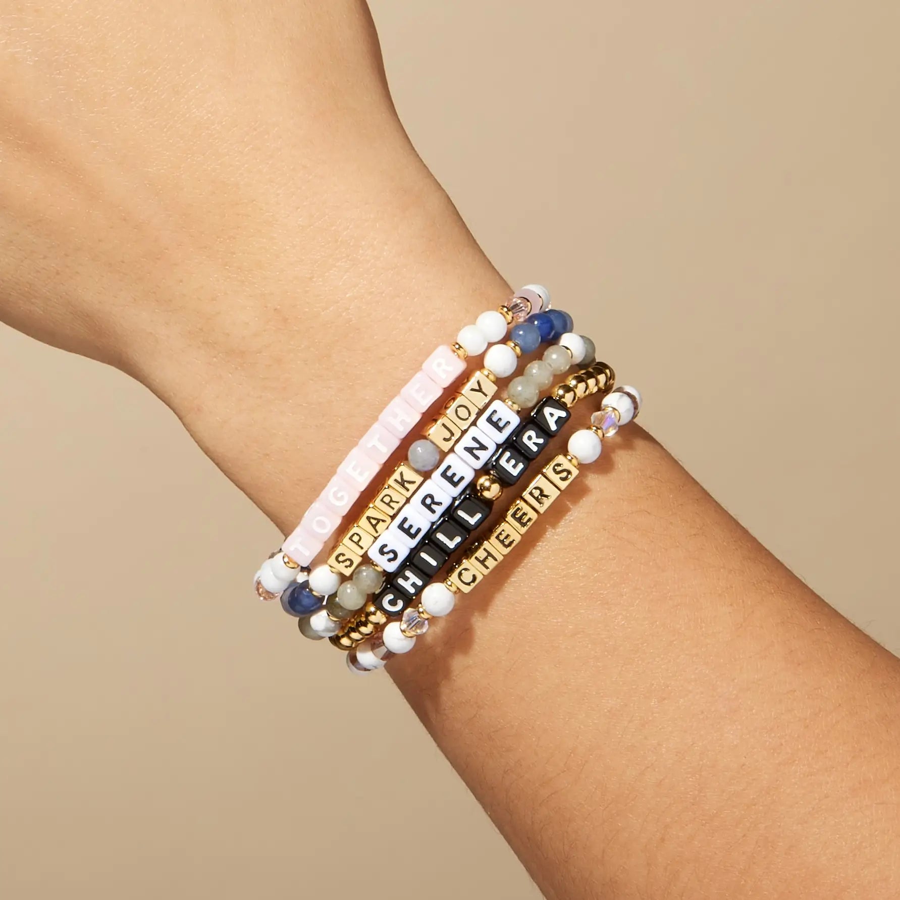 Stack of beaded bracelets with motivational phrases on a wrist against a beige background