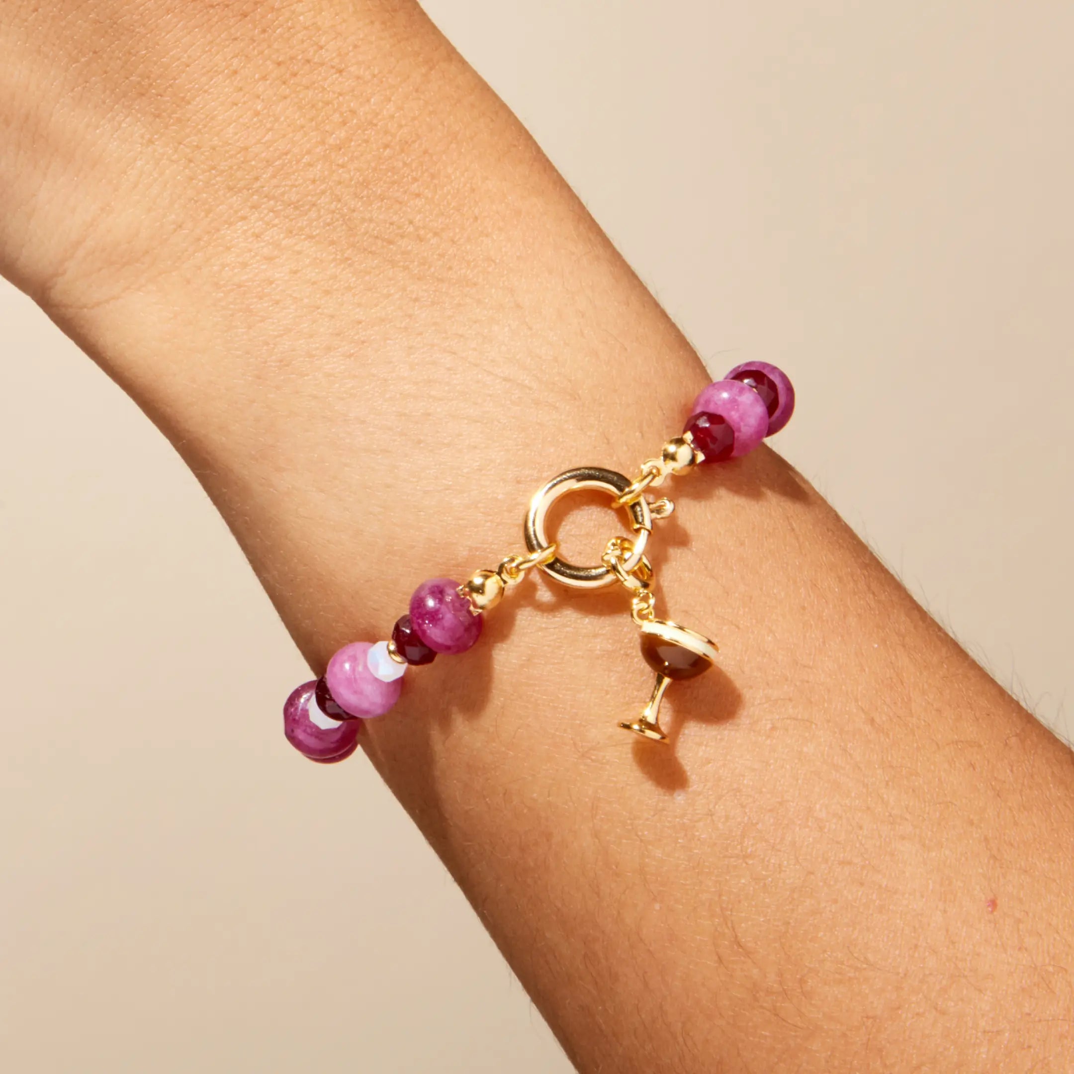 Bracelet with pink beads and gold charm on a wrist against a beige background