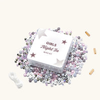 Girls Night In Bead Kit tin surrounded by its contents: white letter beads, lilac, mauve, gray and speckled stone beads, iridescent crystals, gold closure beads, and elastic stretch string, flat-lay on cream background