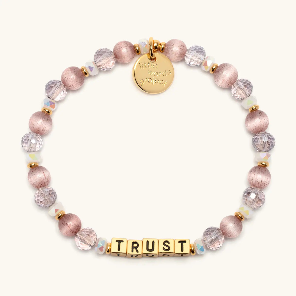 Trust bracelet with gold letter beads in the Grace in Motion bead pattern, mauve satin beads, blush faceted crystals, and small white beads with gold accents, flat-lay on cream background