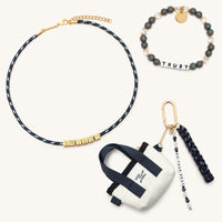 Fall Founder Faves Set flat-lay on cream background showing the Trust bracelet in white letter beads with gray speckled and clear crystal beads, the BOLDER Enough paracord necklace in navy with gold CZ letter blocks, and the Do Your Best Bag Charm with mini canvas tote, navy paracord tassel, and pearl beaded word strand