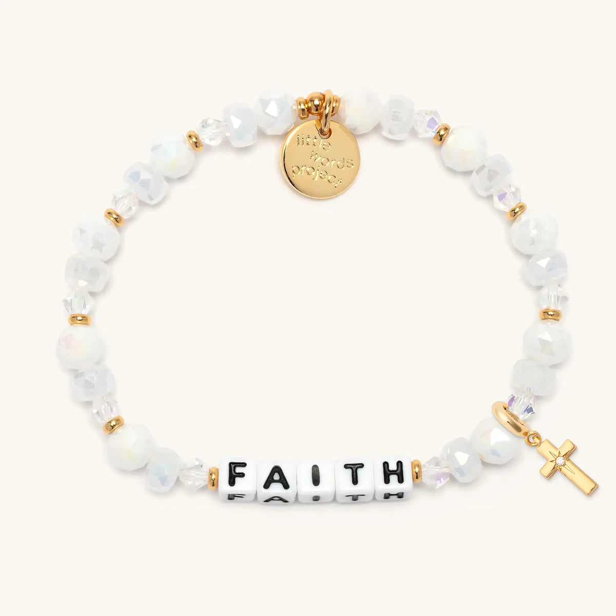 Faith bracelet in the Snowflake Sparkle bead pattern with white letter beads, gold puffy cross charm with a clear CZ stone, flat-lay on cream background