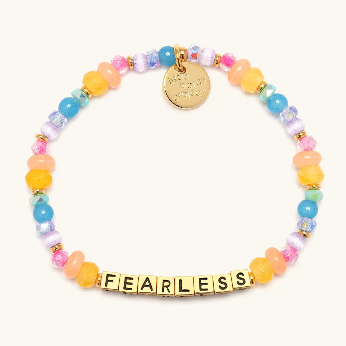 Fearless- Britt Horton bracelet in the Gemstone Glow bead pattern, gold letter beads with yellow, peach, blue, lavender, and pink semi precious stone, crystal, glass, and cat eye beads with gold accents, flat-lay on cream background