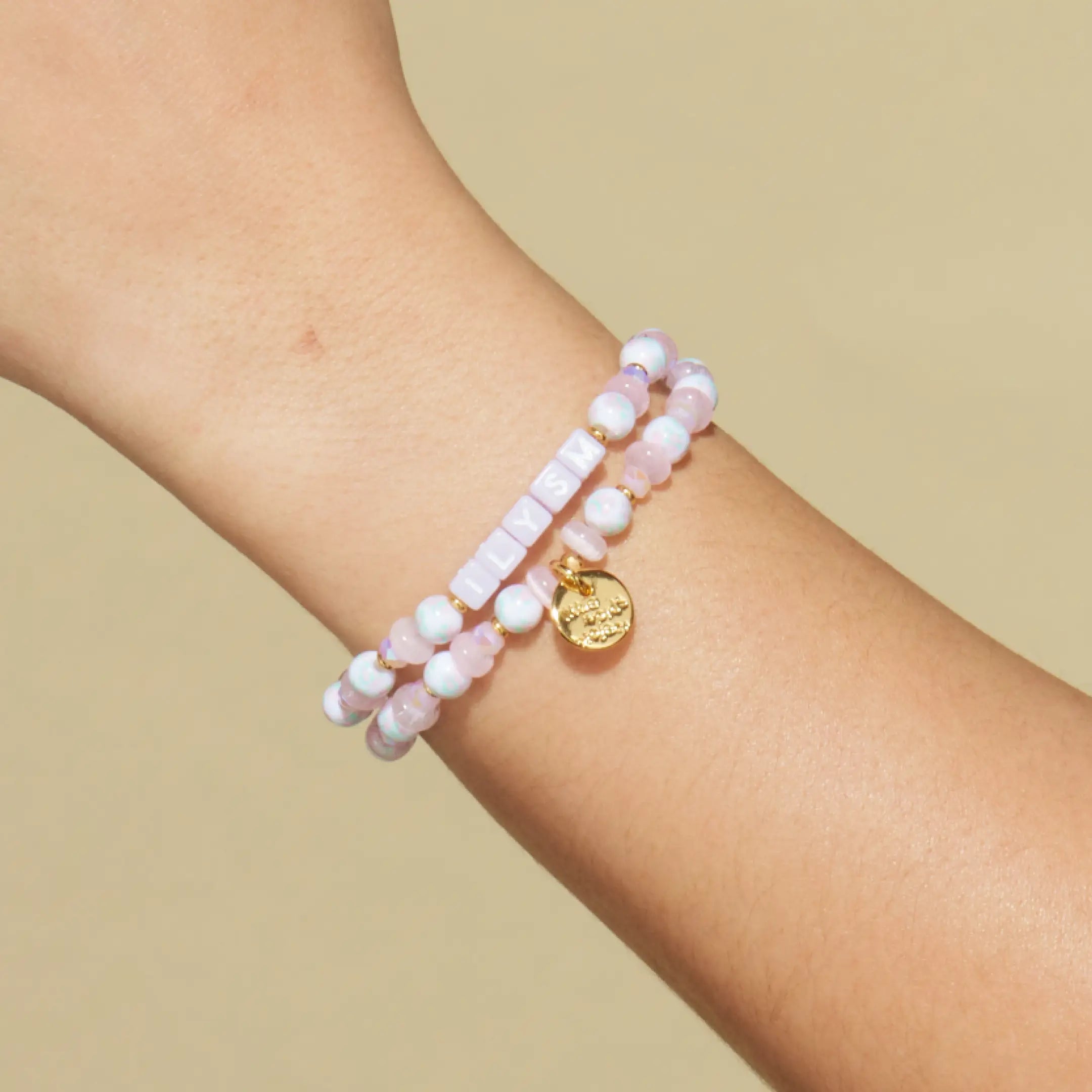 Pink beaded bracelet with a gold tag on a wrist against a beige background