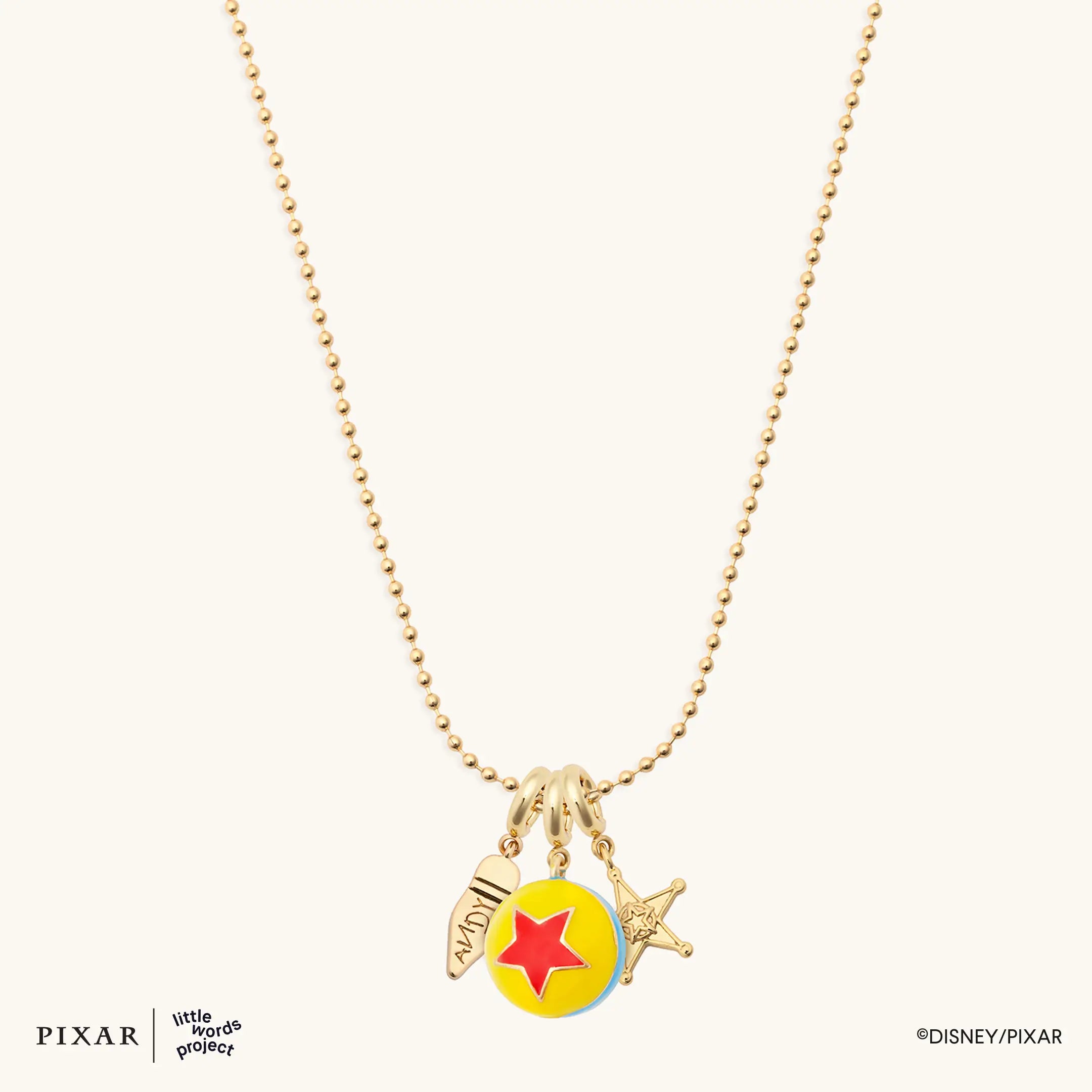 Reach for the Sky Toy Story charm necklace, gold ball-chain with Pixar ball, sheriff star and boot charms, flat lay