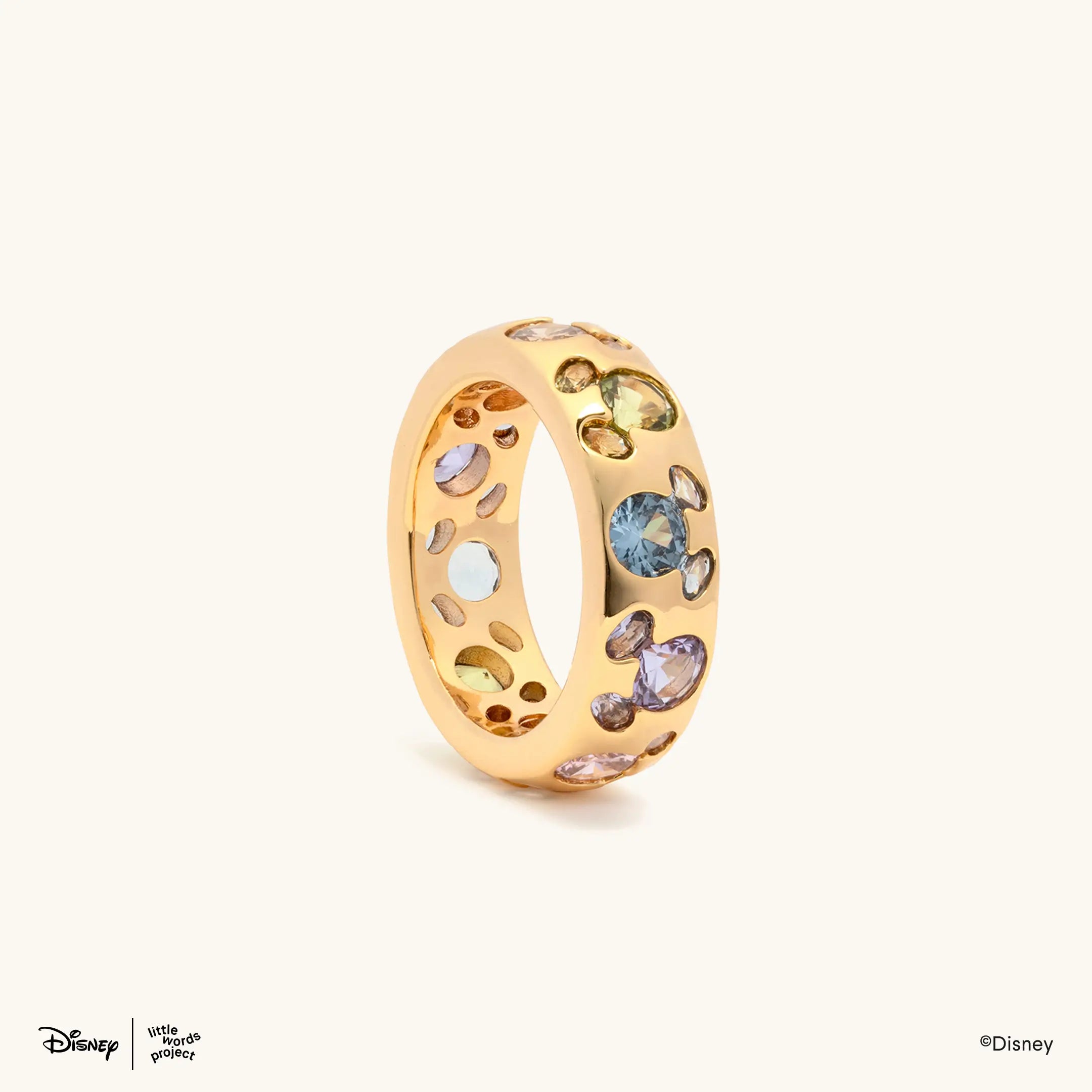 Mickey Mouse Rainbow Ring from Disney Mickey and Friends, gold plated band set with multicolor crystals, angled side view on cream