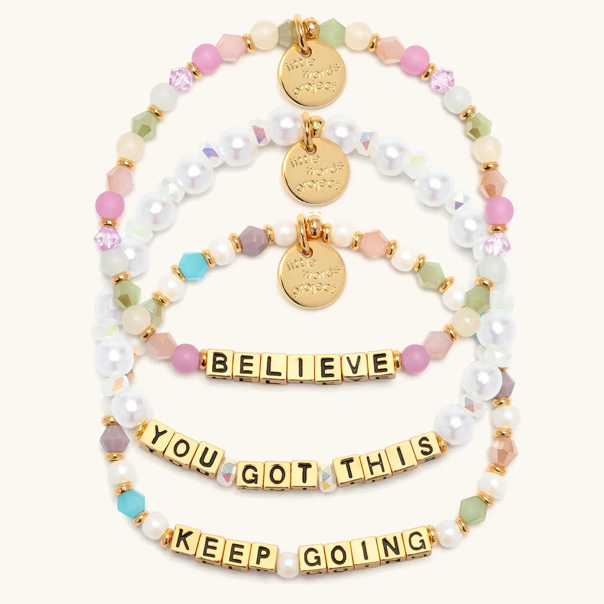 Good Things Ahead Bracelet Set in gold letter beads, flat-lay on cream background showing three stacked bracelets: Believe in orchid, mint and blush beads, You Got This in white faux pearls and iridescent crystals, and Keep Going in pearls and jewel tone crystals