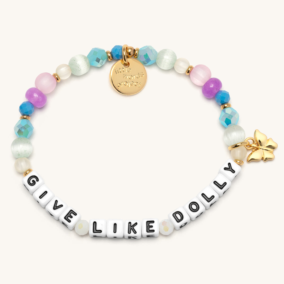 Give Like Dolly Charm Bracelet with white letter beads reading Give Like Dolly, aqua and blue AB crystals, mint cat's eye beads, pink and purple frosted beads, and a gold butterfly charm with gold accents, flat-lay on cream background