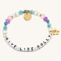 Give Like Dolly Charm Bracelet with white letter beads reading Give Like Dolly, aqua and blue AB crystals, mint cat's eye beads, pink and purple frosted beads, and a gold butterfly charm with gold accents, flat-lay on cream background