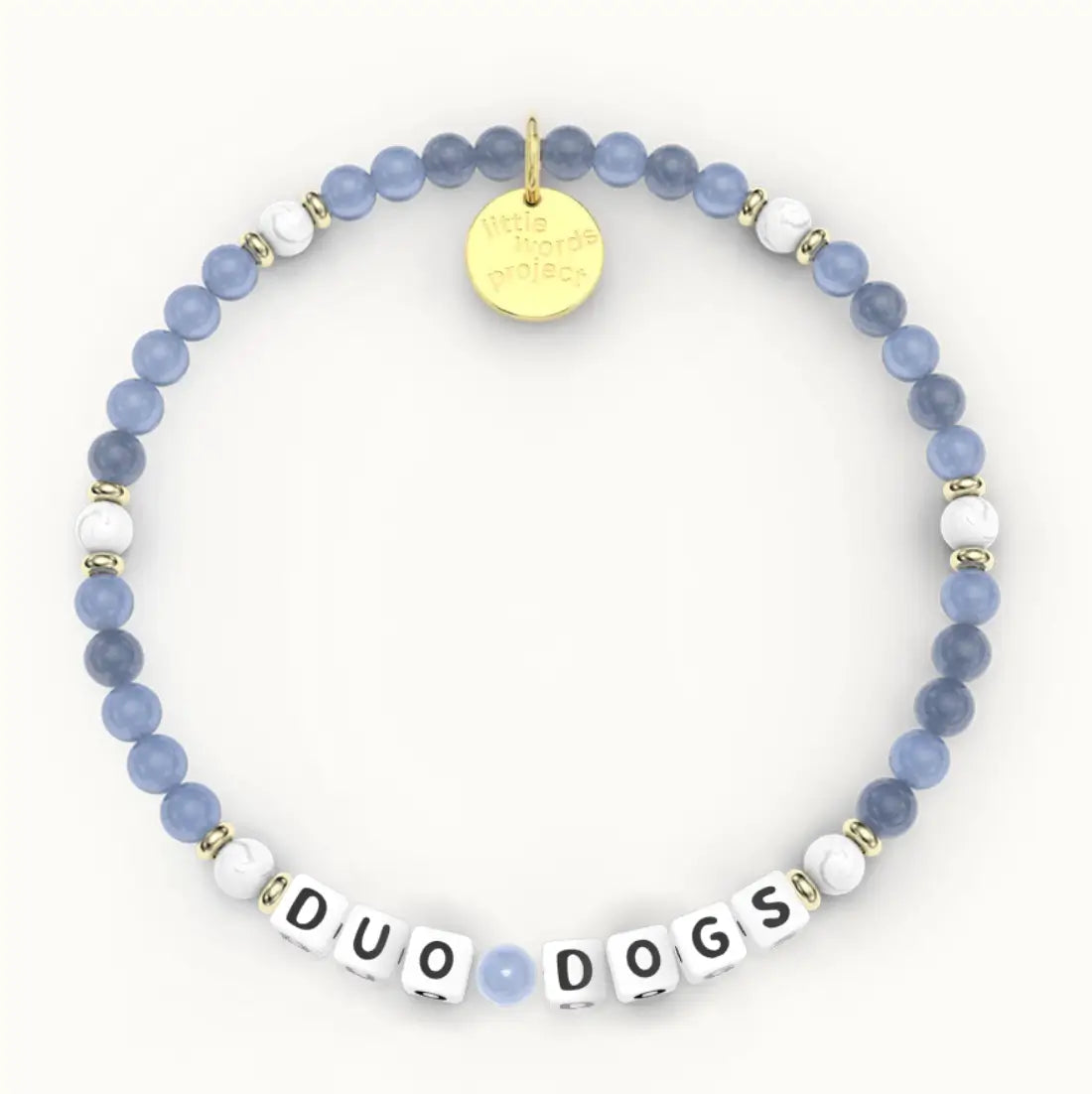 Duo Dogs giveback bracelet in the Bluestone bead pattern, white letter beads with blue stone and white howlite beads with gold accents, flat-lay on cream background
