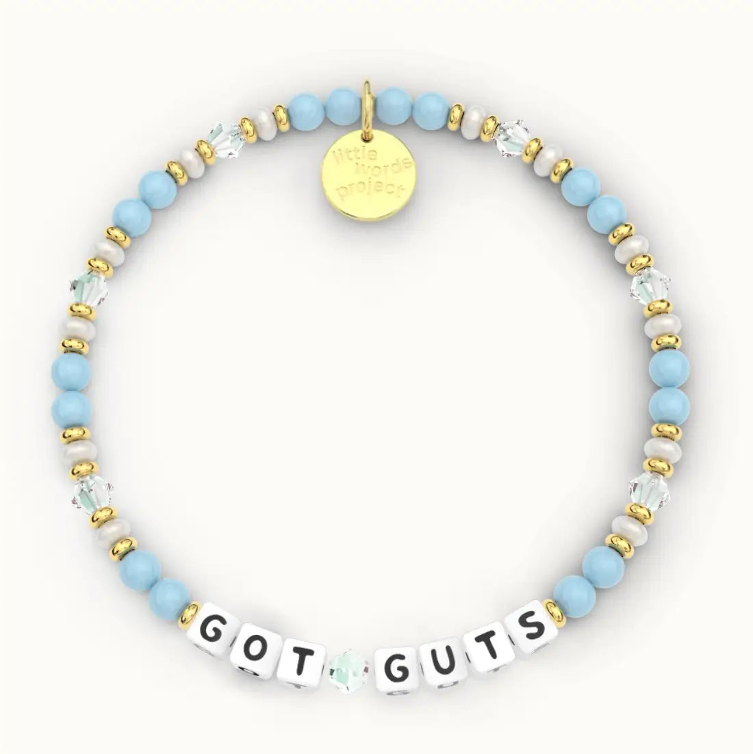 Got Guts giveback bracelet in the Chambray bead pattern, white letter beads with light blue beads, white pearls and clear crystal beads with gold accents, flat-lay on cream background