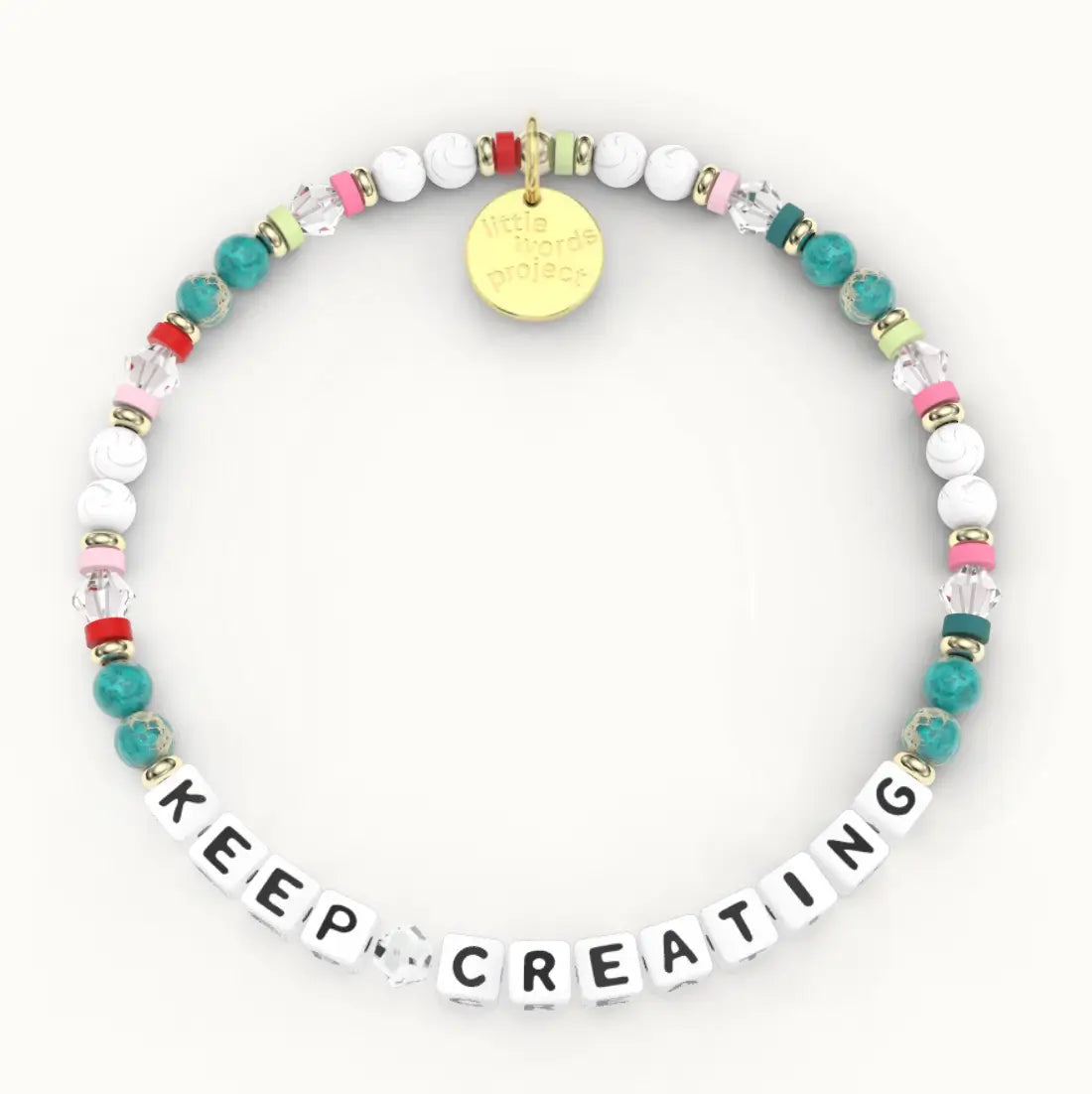 Keep Creating giveback bracelet in the Joyful bead pattern, white letter beads with teal stone, white howlite and clear crystal beads and pink, green and red spacers with gold accents, flat-lay on cream background