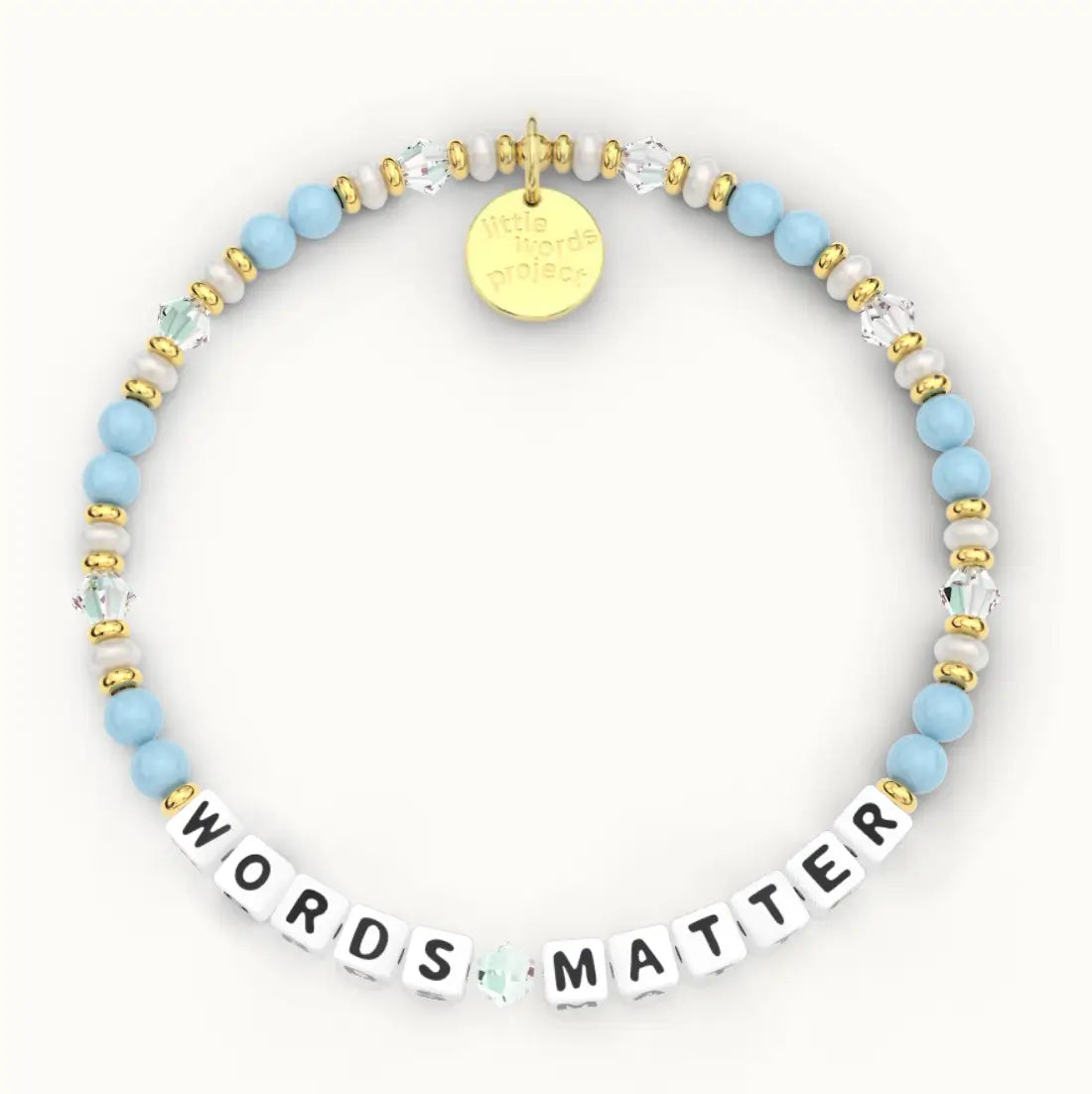 Words Matter giveback bracelet in the Chambray bead pattern, white letter beads with light blue beads, white pearls and clear crystal beads with gold accents, flat-lay on cream background