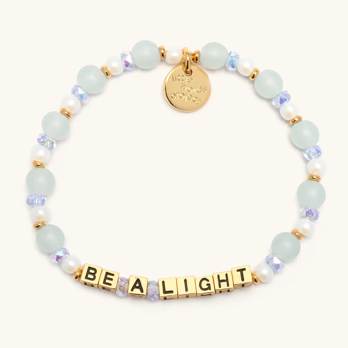 Gold Be a Light bracelet in the Honeydew Kiss bead pattern, gold letter beads with seafoam glass beads, white faux pearls, and periwinkle iridescent crystals with gold accents, flat-lay on cream background