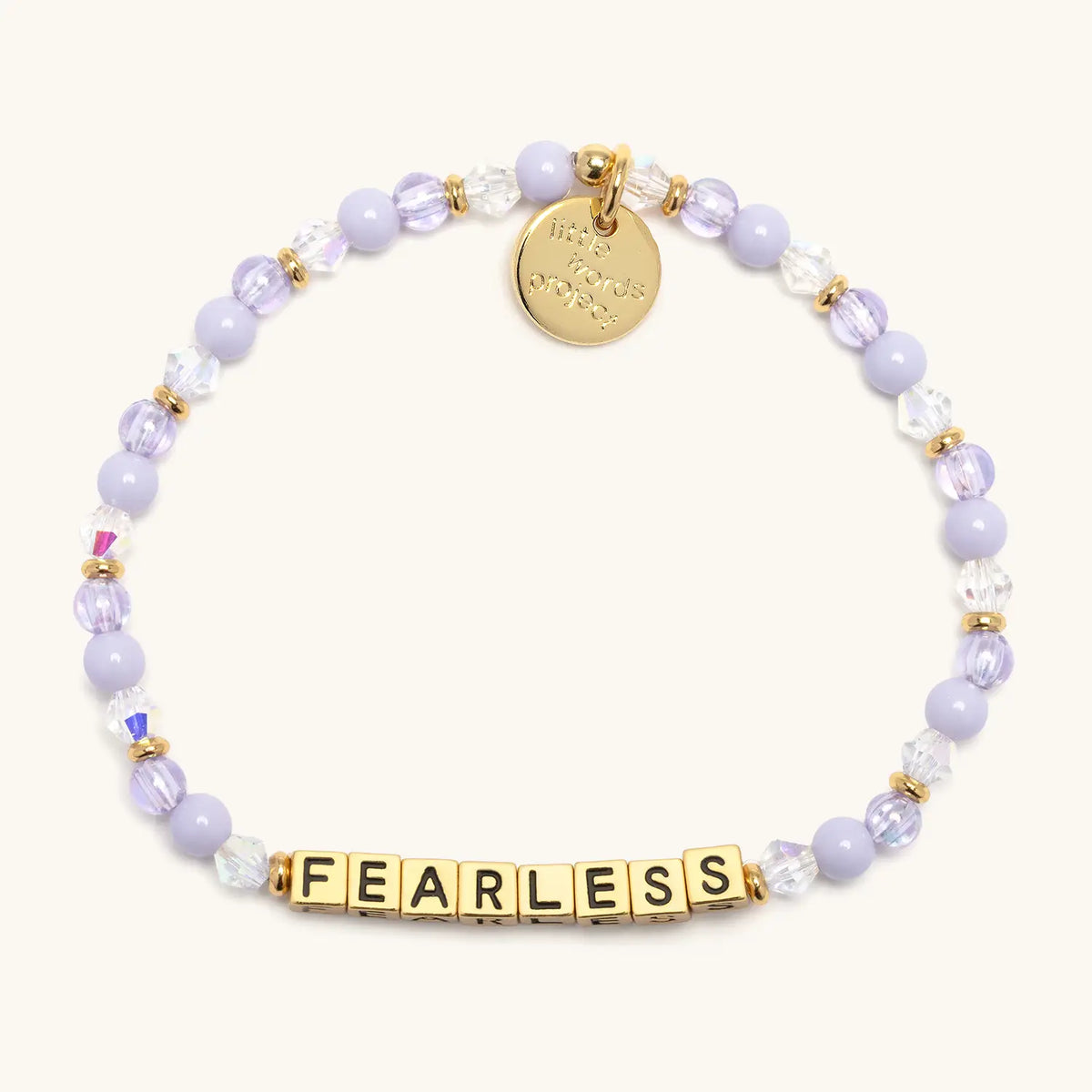 Gold Fearless bracelet in the Purple Haze bead pattern, gold letter beads with lavender pearls and clear and lilac faceted crystals with gold accents, flat-lay on cream background