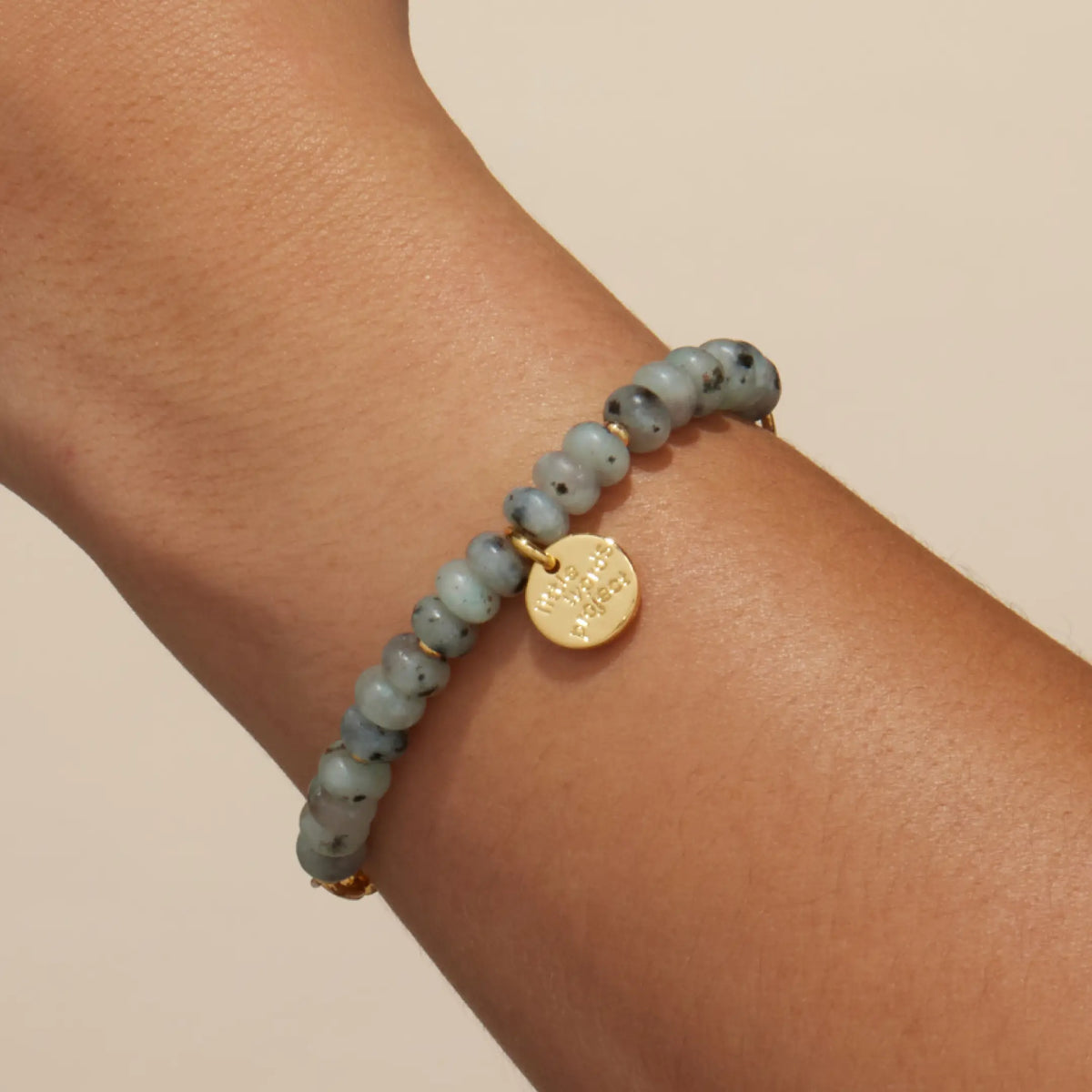 Smoky Ink Bracelet Base worn on a wrist, showing the gold link chain half of the half beaded, half chain bracelet, on-model on a tan background