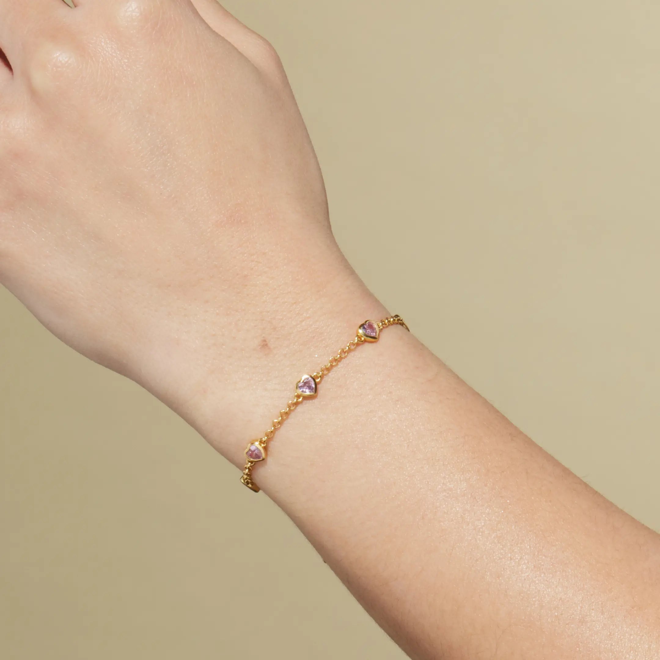 Gold bracelet with heart-shaped gems on a wrist against a beige background