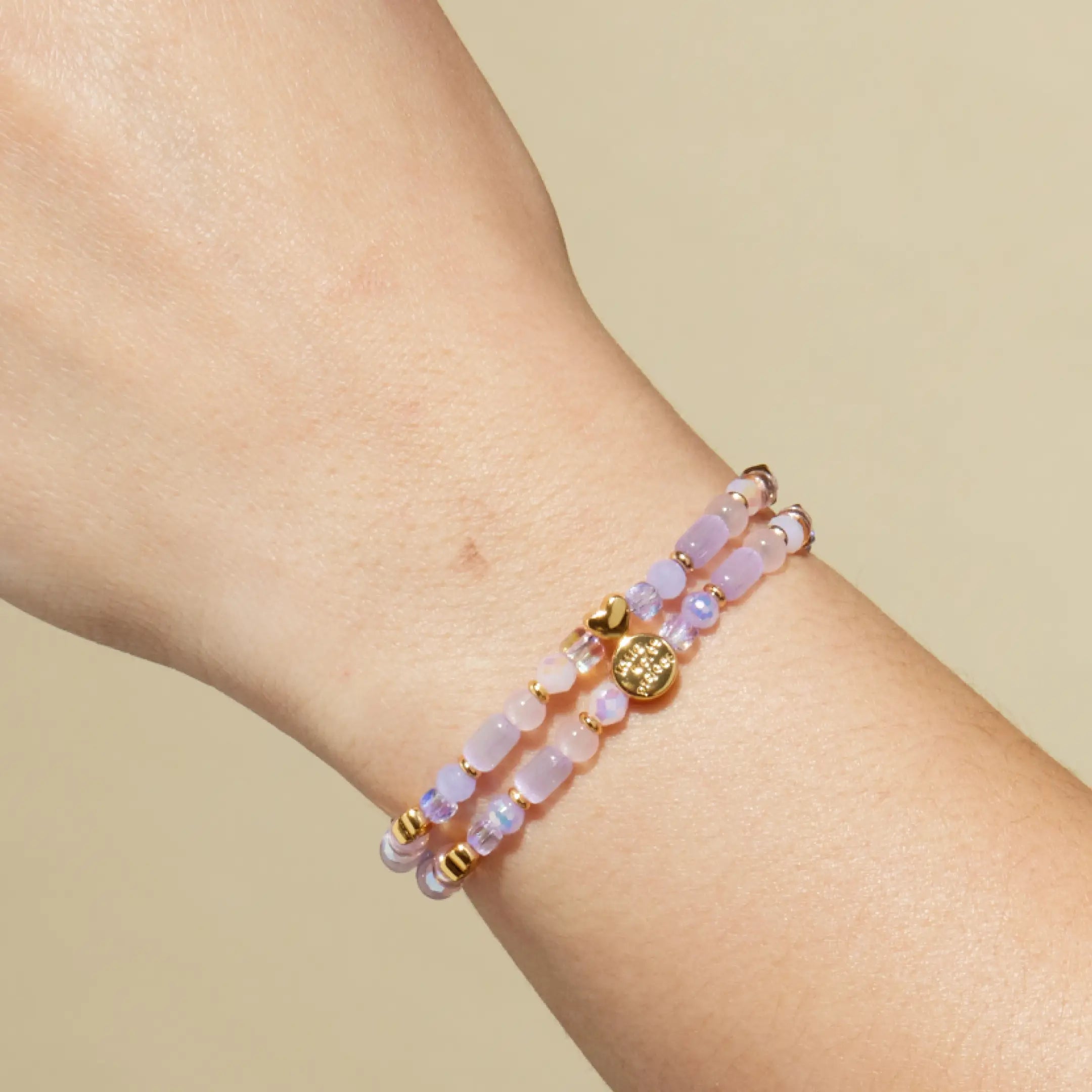 Bracelet with pink beads and gold accents on a wrist against a beige background