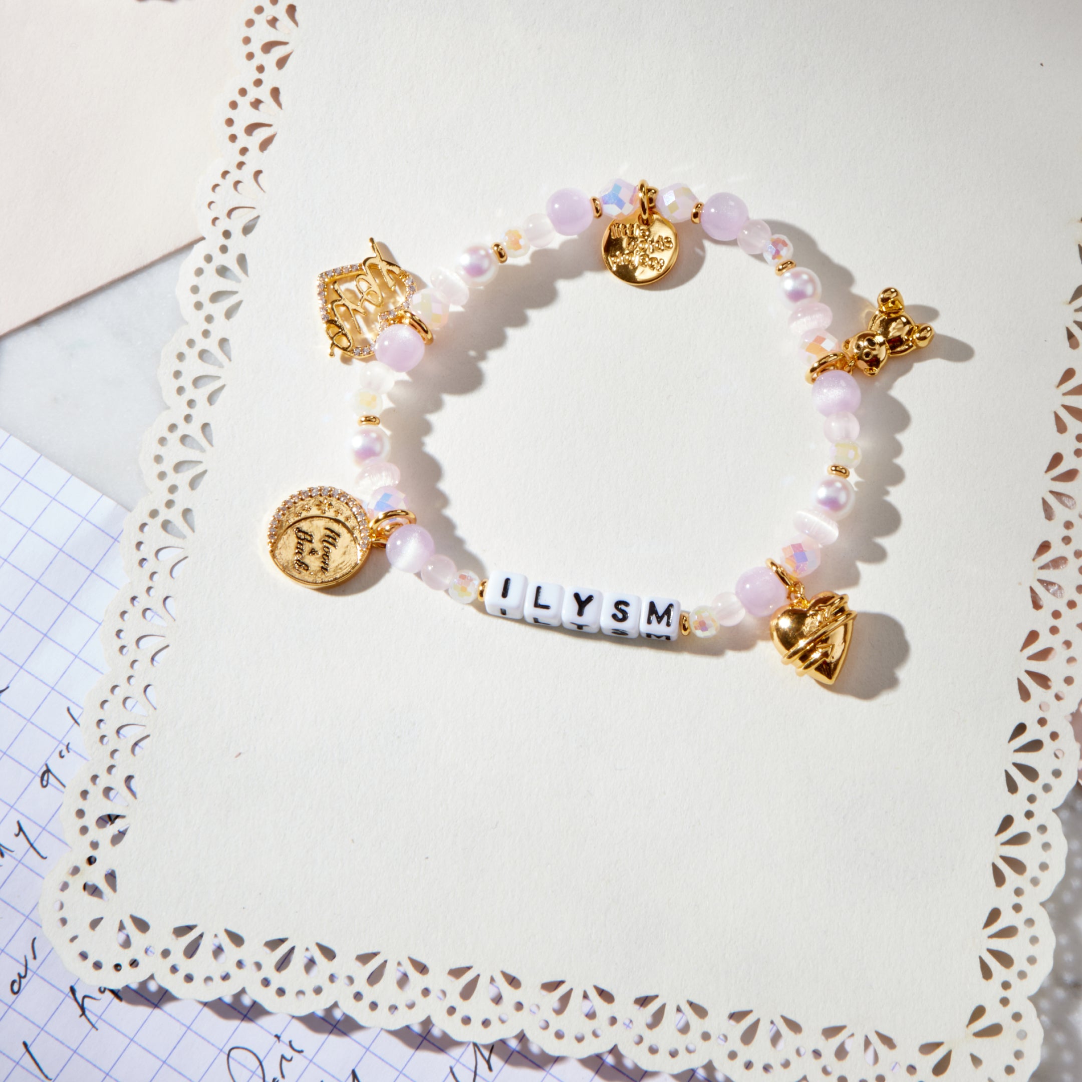Bracelet with pink beads and gold charms on a decorative white doily card