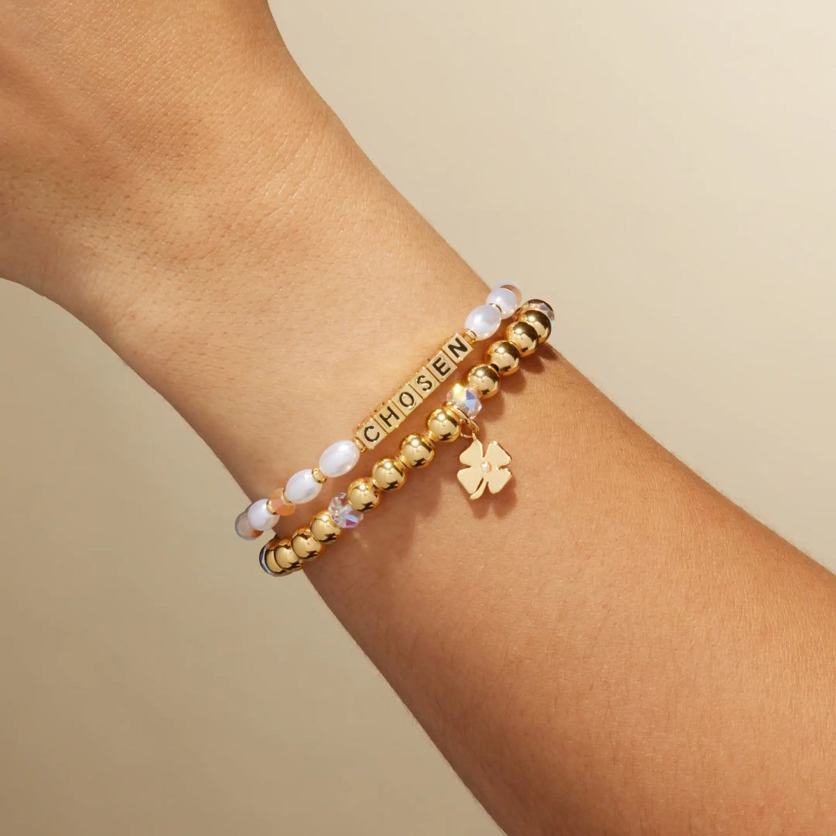 Chosen Bracelet Set by Kirstin Czernek on-model on wrist, the Chosen bracelet with white faux pearls and gold letter beads stacked with the gold beaded Four Leaf Clover Charm Bracelet