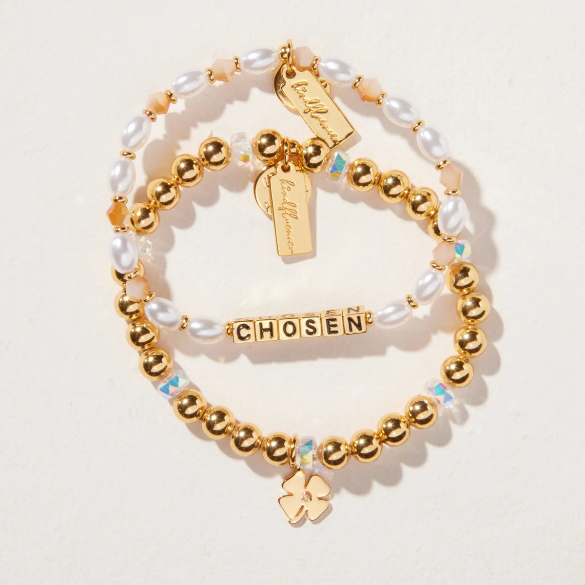 Chosen Bracelet Set by Kirstin Czernek flat-lay on light background, the Chosen bracelet with white faux pearls and gold letter beads stacked with the gold beaded Four Leaf Clover Charm Bracelet