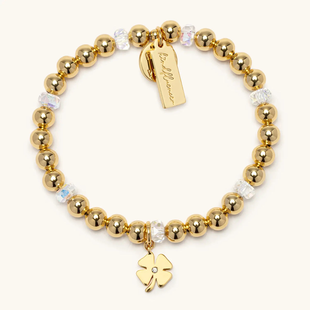Four Leaf Clover Charm Bracelet by Kirstin Czernek, 6mm gold plated beads with clear crystals and a gold four leaf clover charm, flat-lay on cream background